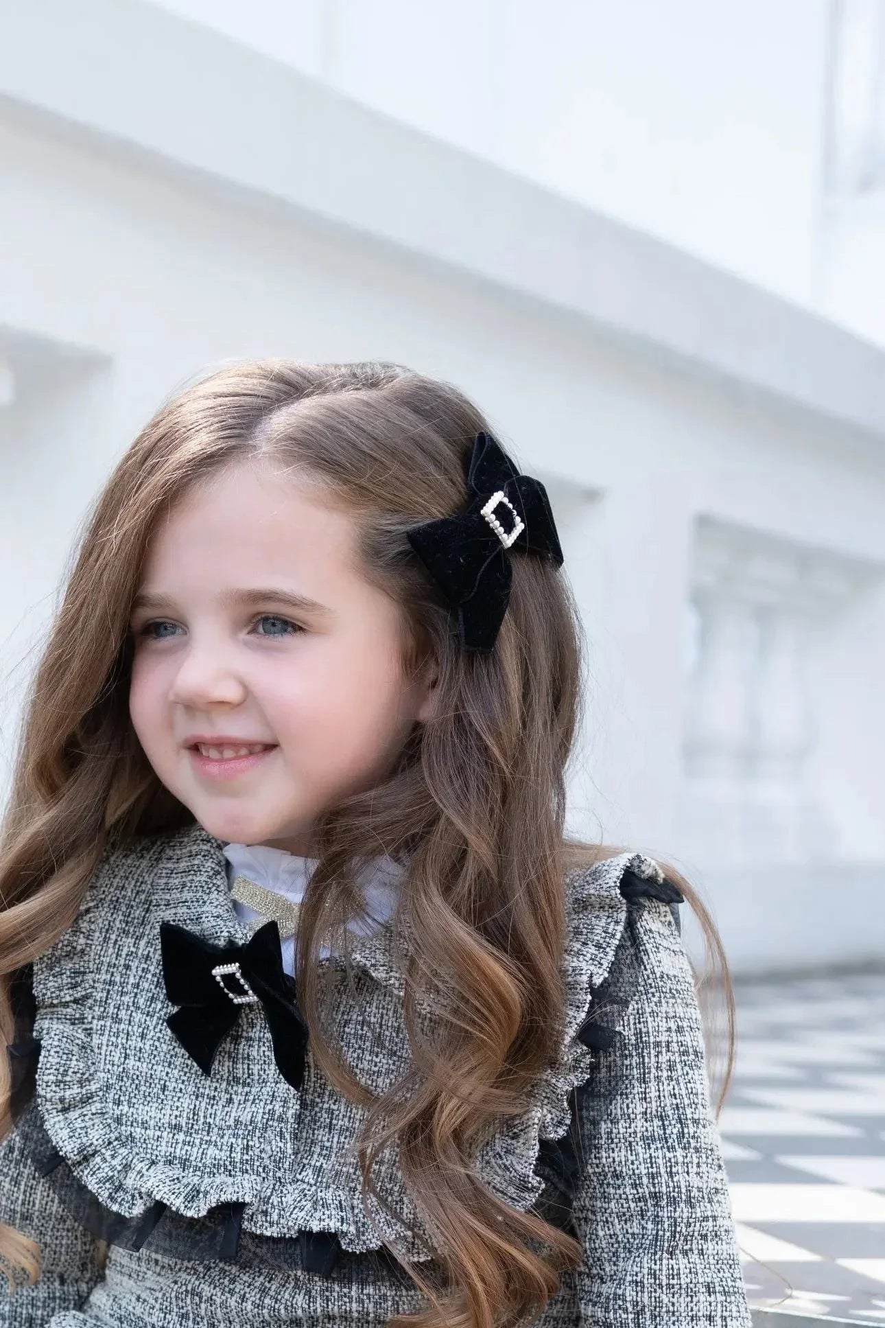 Young girl with long wavy hair wearing a patterned dress and black velvet bows outdoors