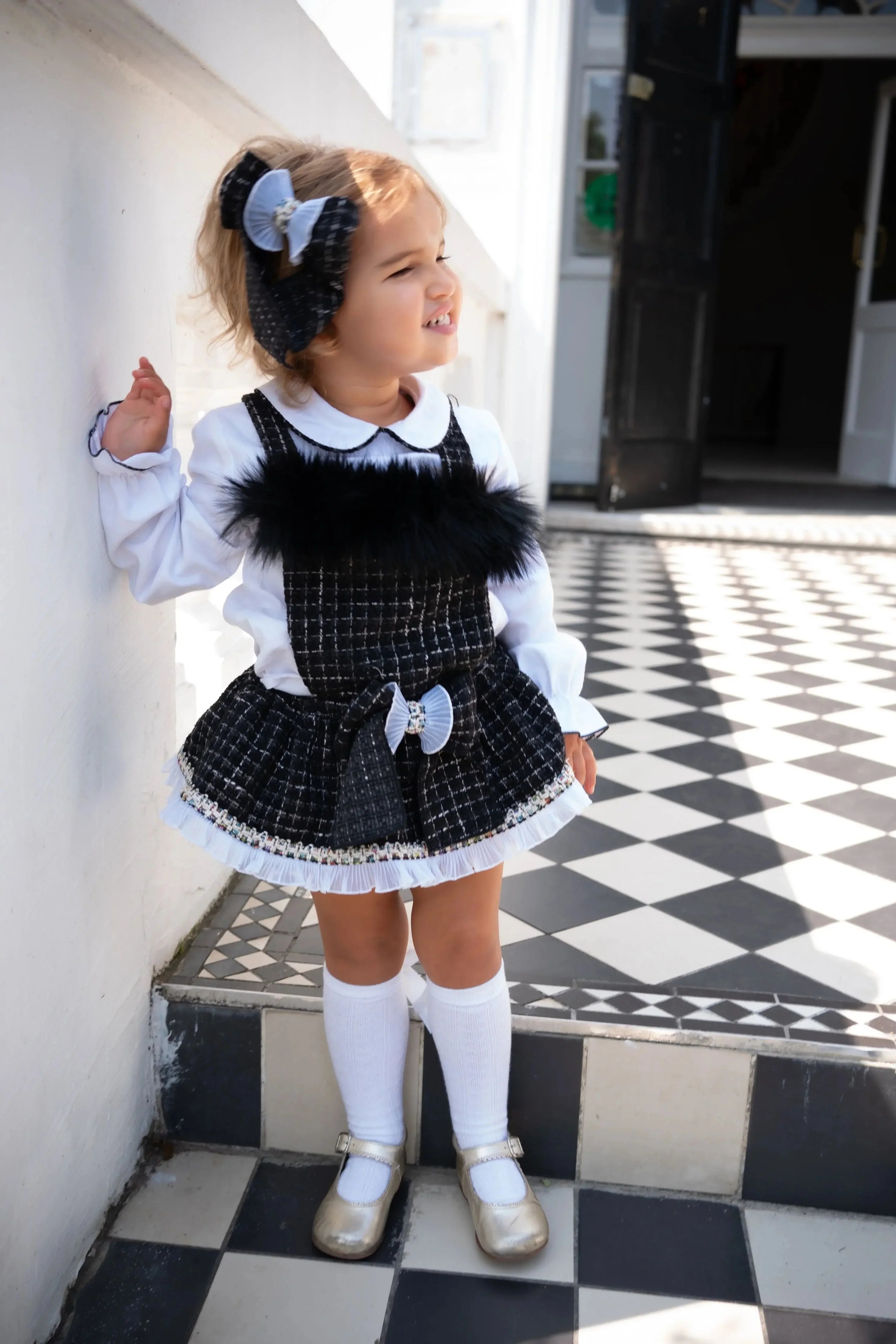 Toddler girl in black and white checkered dress with white blouse, knee-high socks, and gold shoes