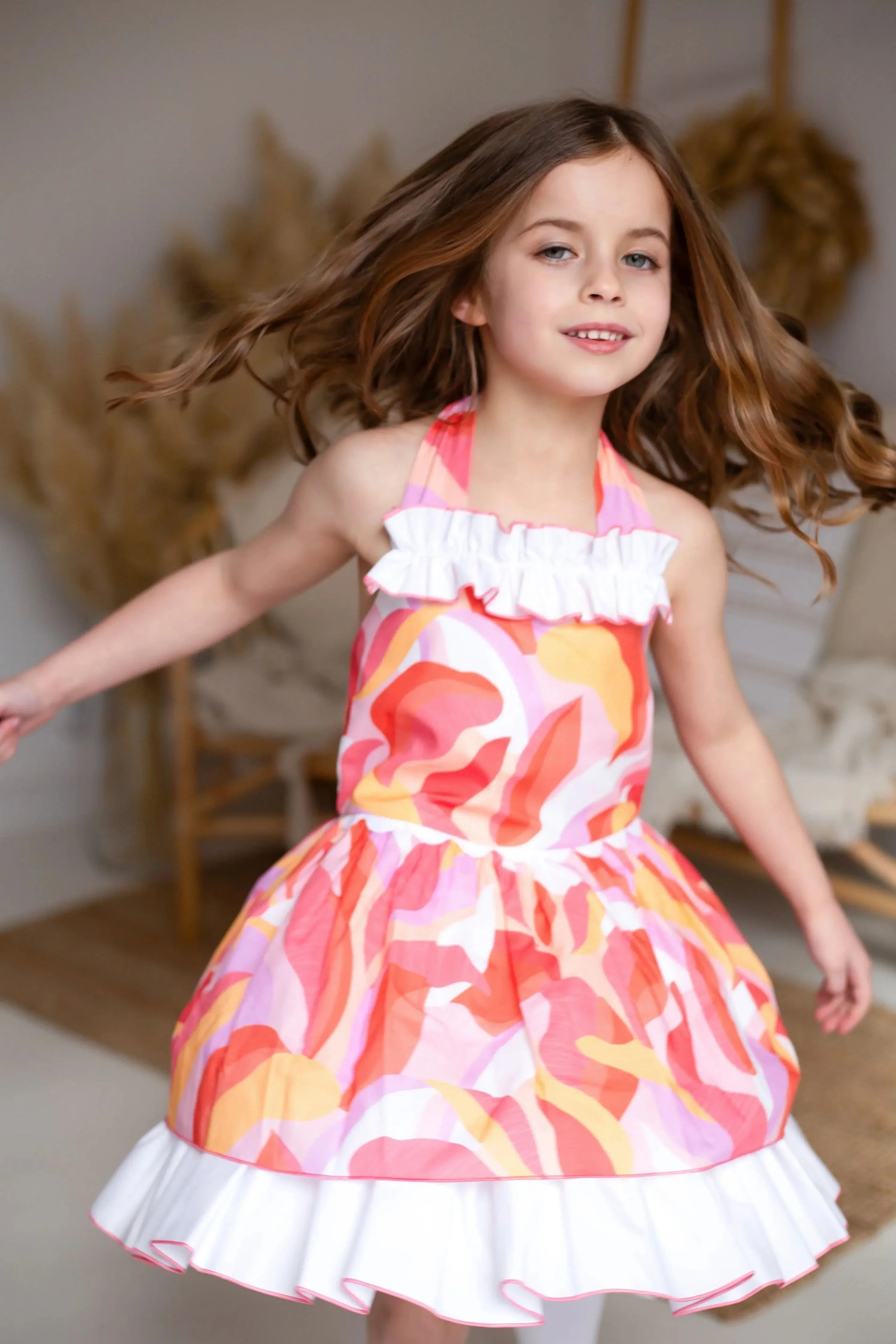 Young girl twirling indoors wearing a colorful swirl patterned dress with white ruffles