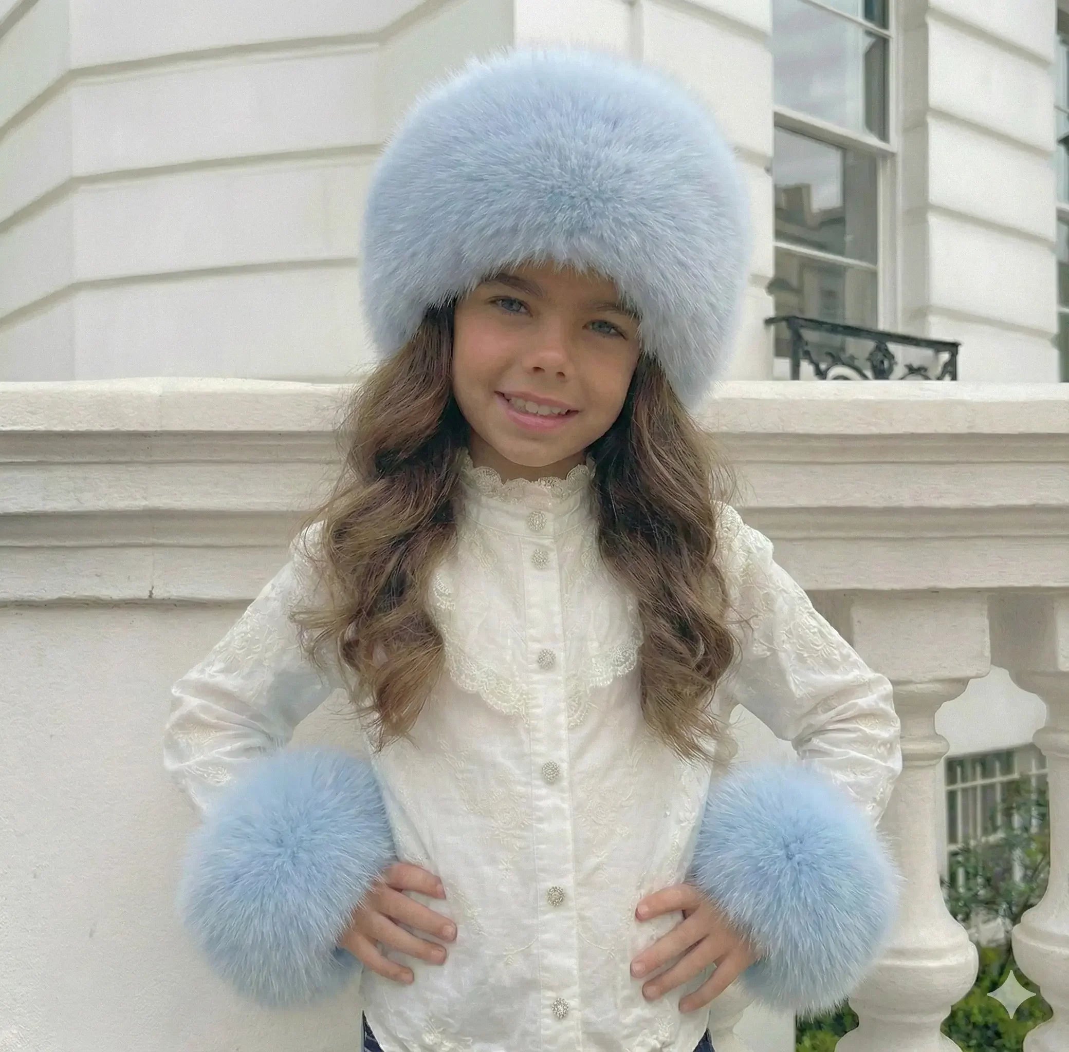 Young girl wearing a white lace blouse with light blue fur hat and matching fur cuffs outdoors