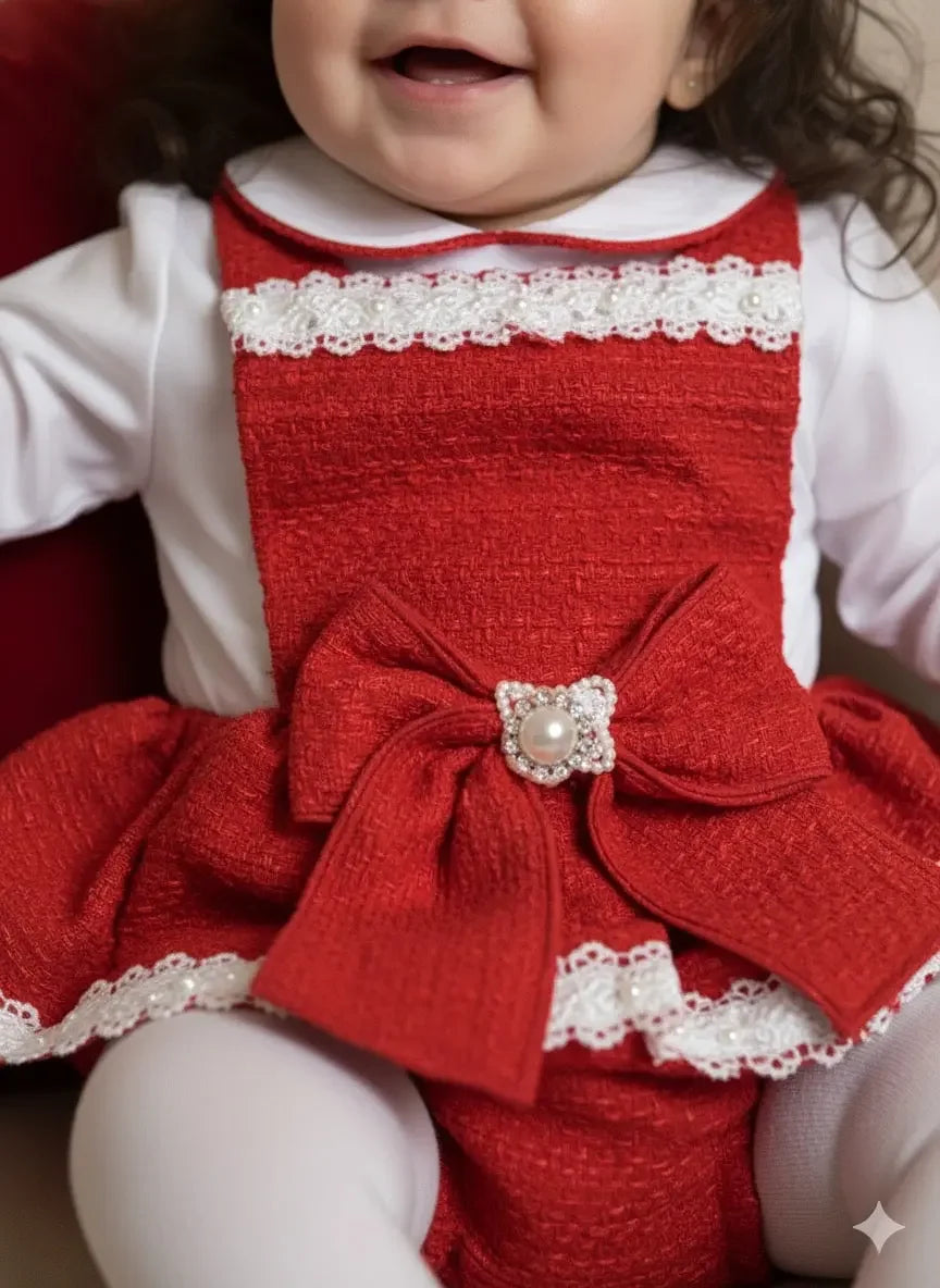 Baby wearing red textured dress with large bow and pearl detail over white long-sleeve shirt