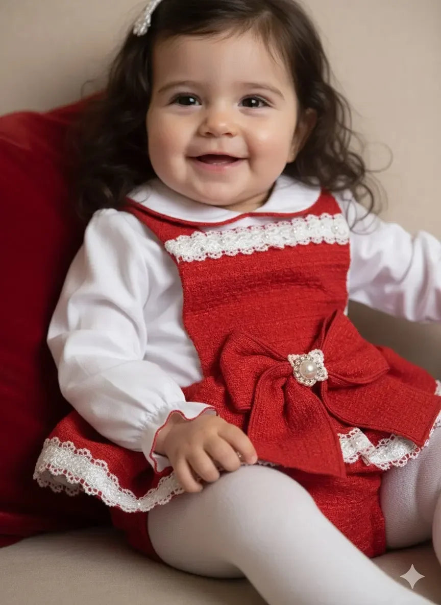 Smiling baby girl in red dress with lace and bow detail sitting on beige chair
