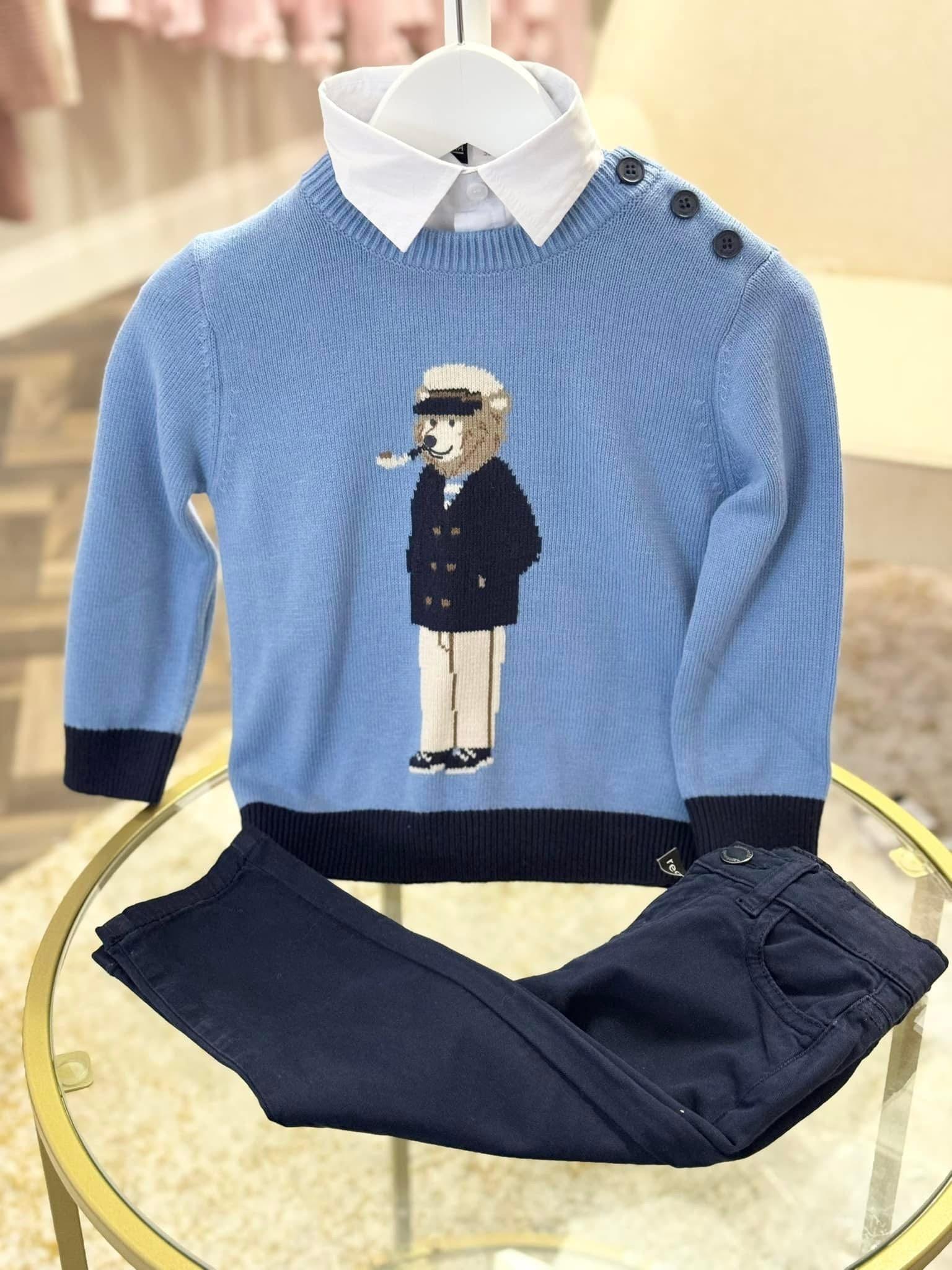 Blue children's sweater with sailor bear design, white shirt collar, and navy blue pants on glass table