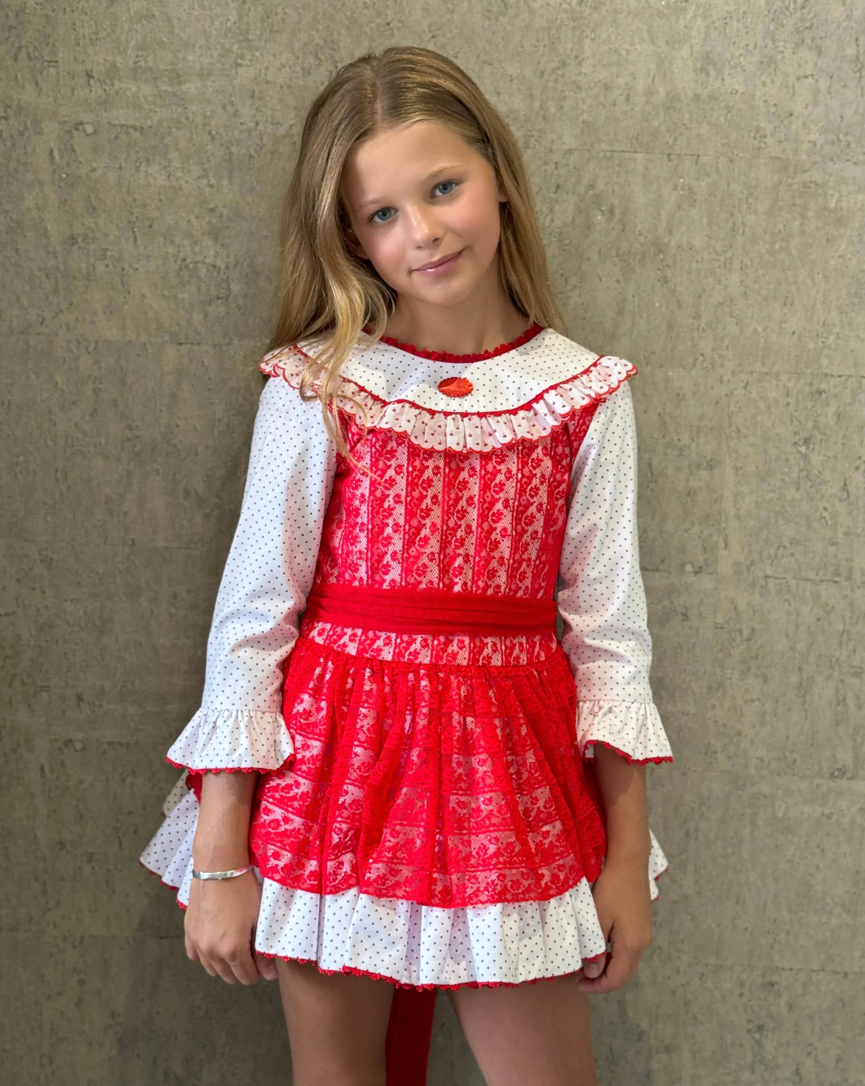 Young girl wearing a red and white vintage dress with lace and polka dots against a textured wall