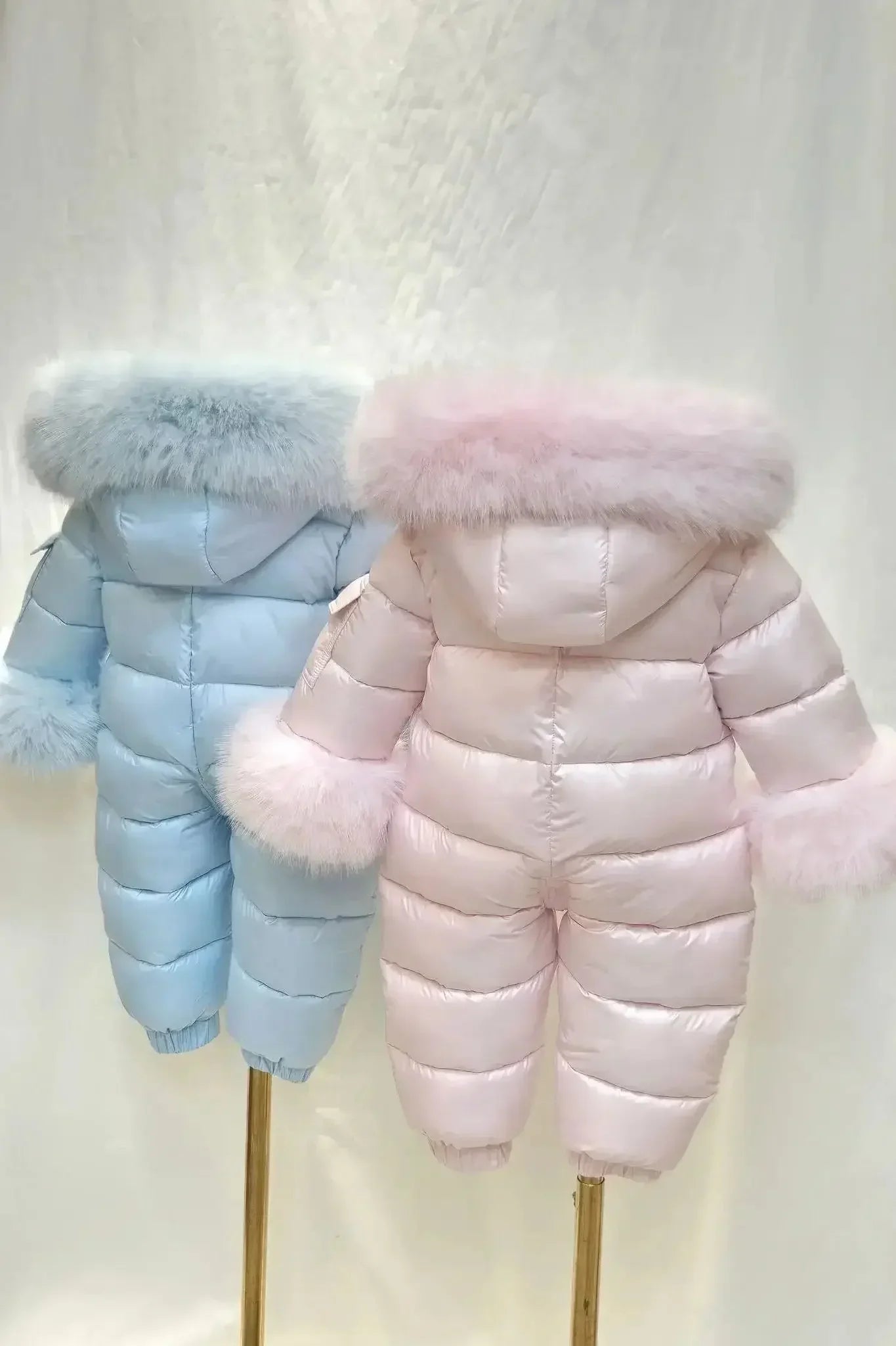 Two puffer winter snowsuits for toddlers with fur trimmed hoods and sleeves in light pink and light blue