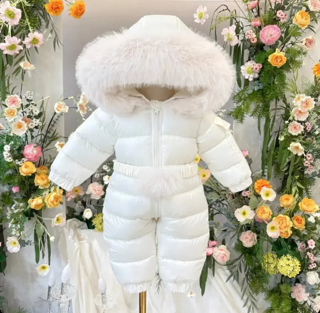 White puffer baby snowsuit with fur-trimmed hood displayed against floral background
