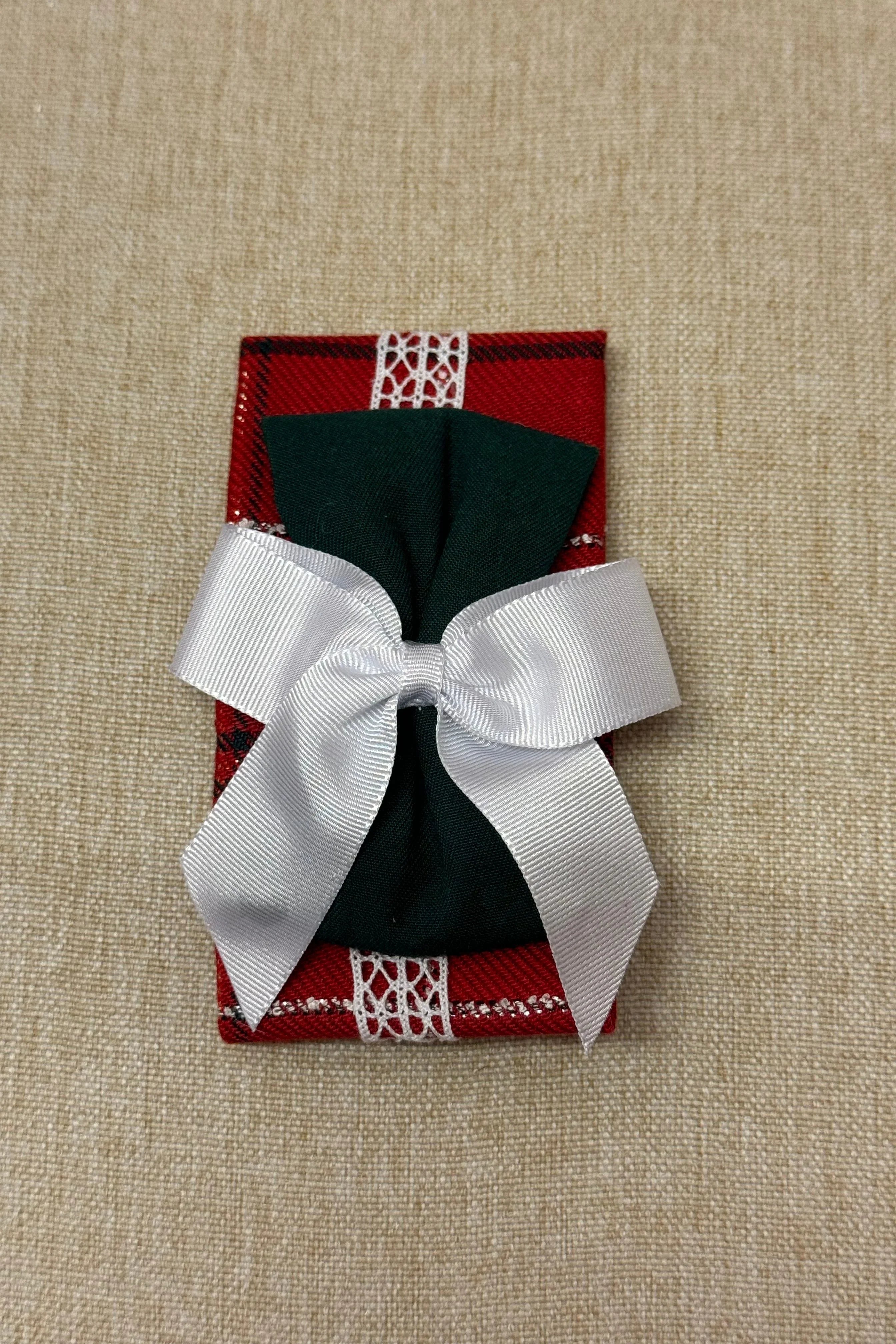 Red check fabric headband with green bow and white ribbon on beige background