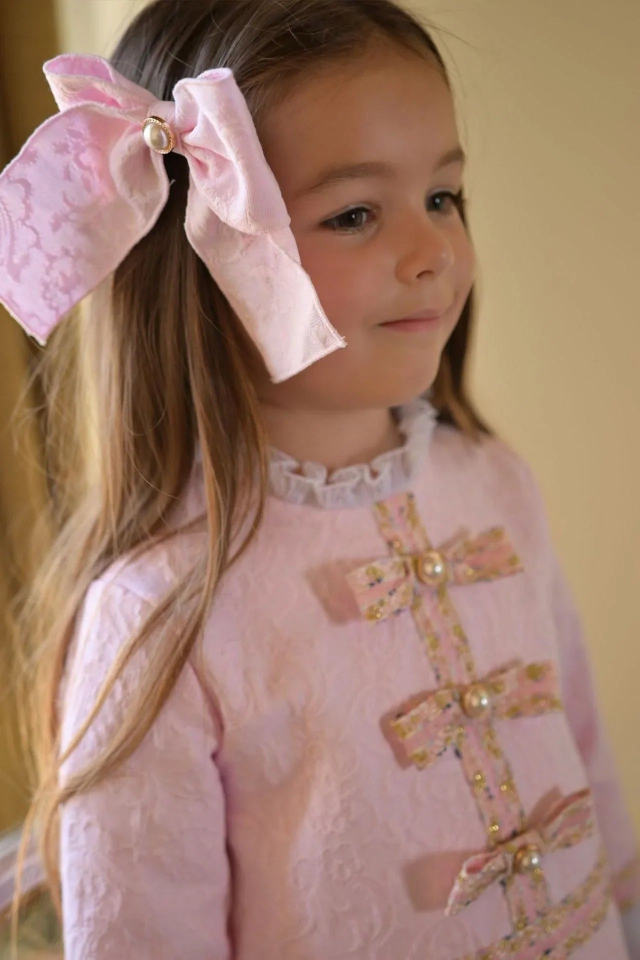 Young girl wearing pink damask dress with pearl and ribbon bows, and a large lace bow in her hair