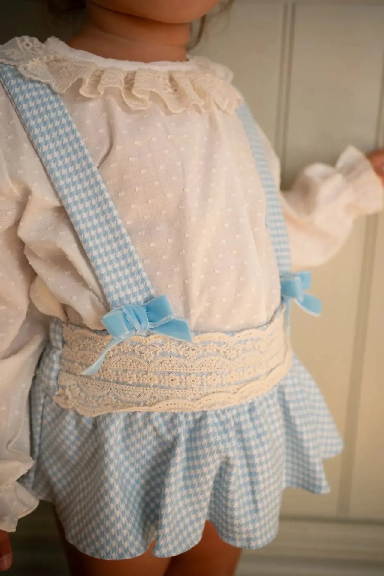 Toddler girl wearing blue gingham jam pant set with lace blouse and suspenders