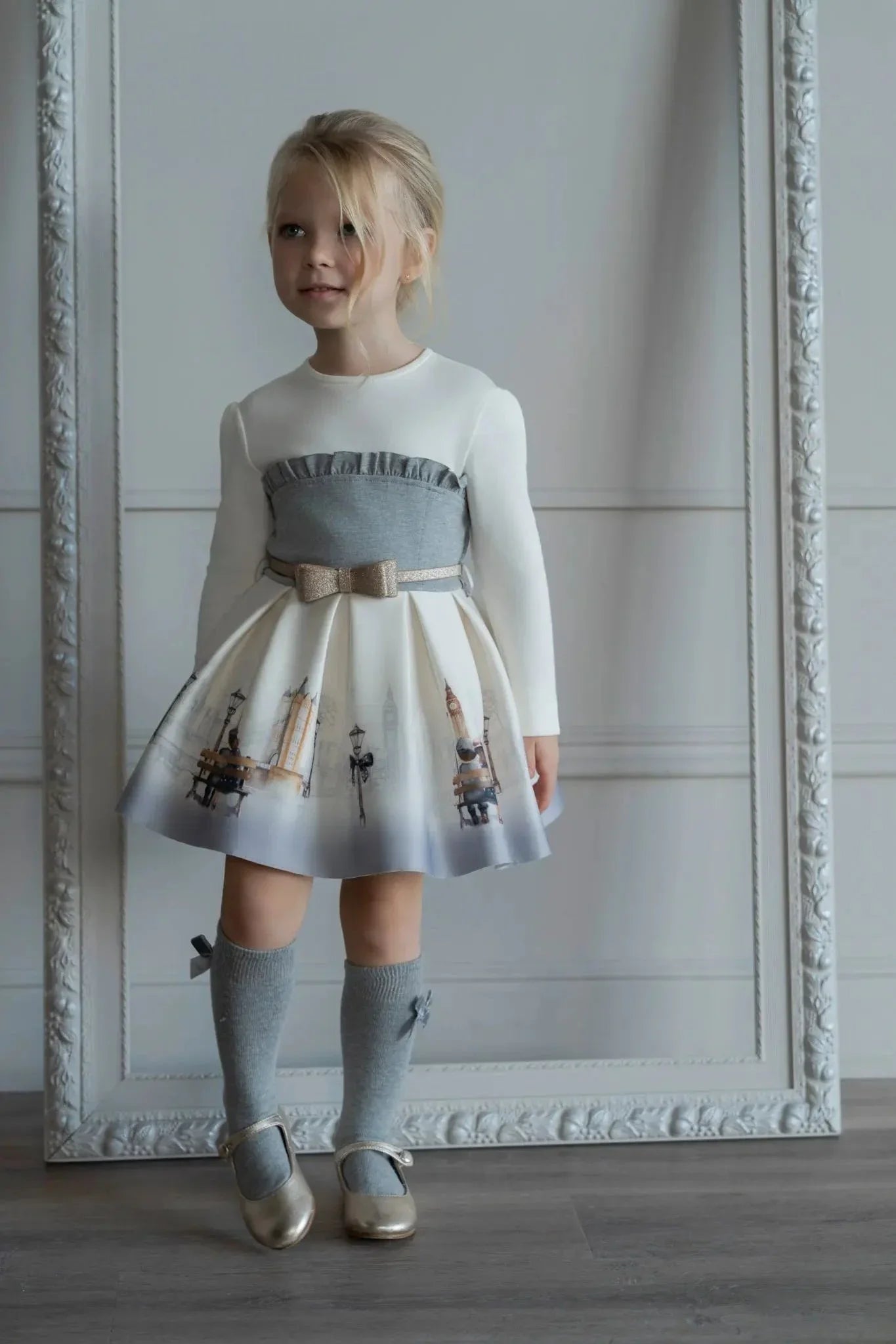 Young girl wearing a white and grey London-themed dress with bow belt, knee socks, and gold shoes