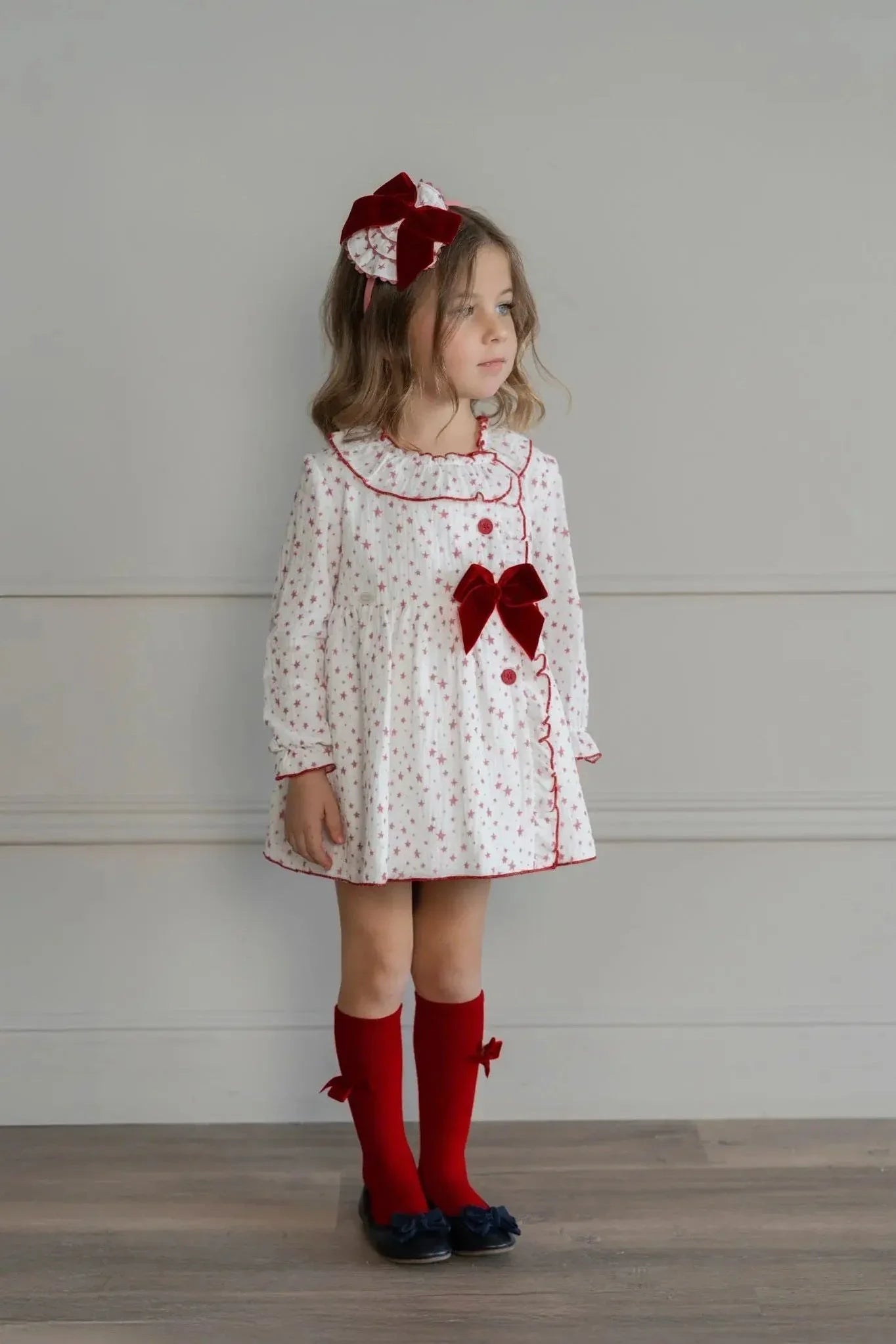 Young girl wearing white dress with red star print, red velvet bows, matching headband and red knee-high socks
