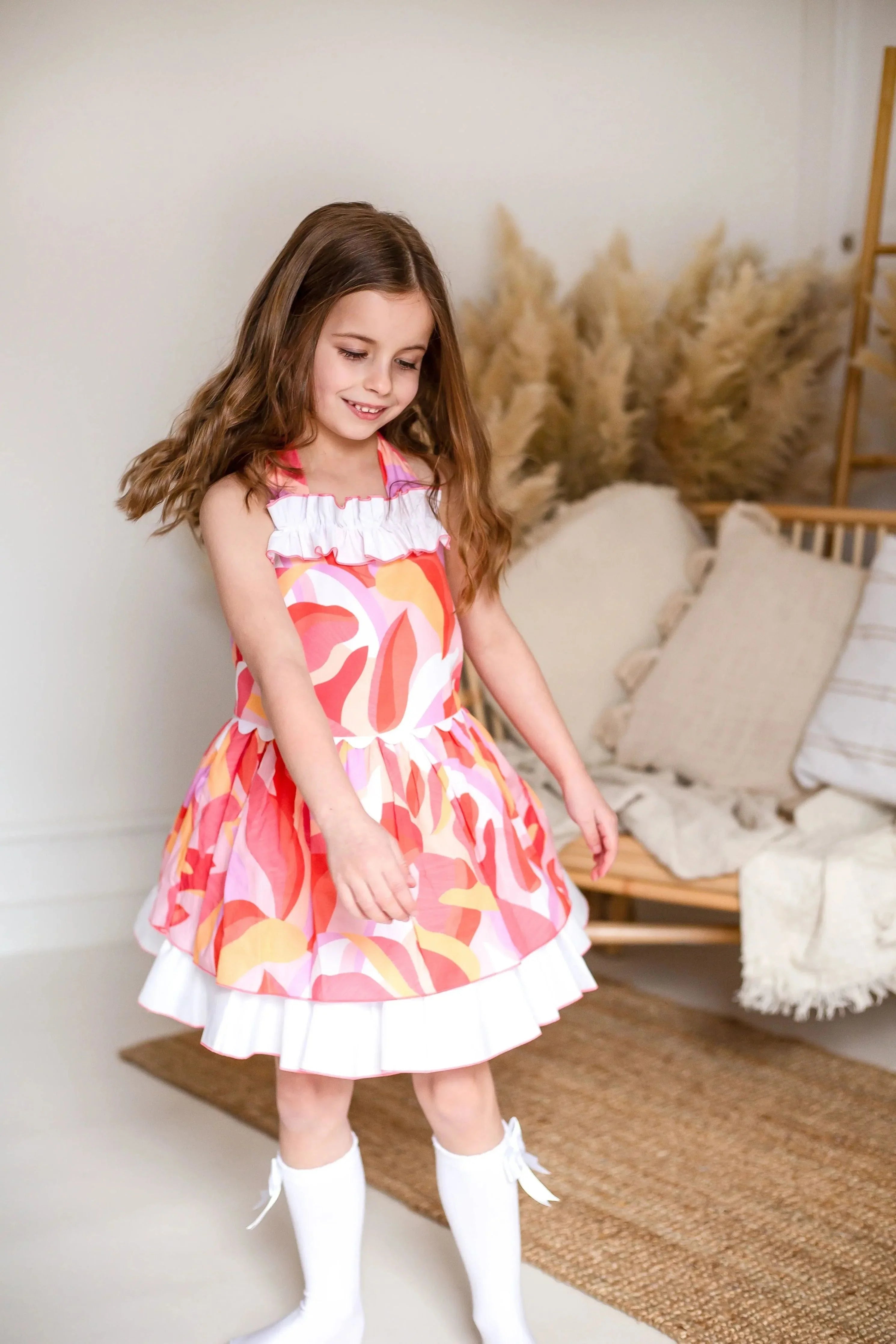 Smiling girl in colorful patterned dress and white knee-high socks indoors with cozy decor