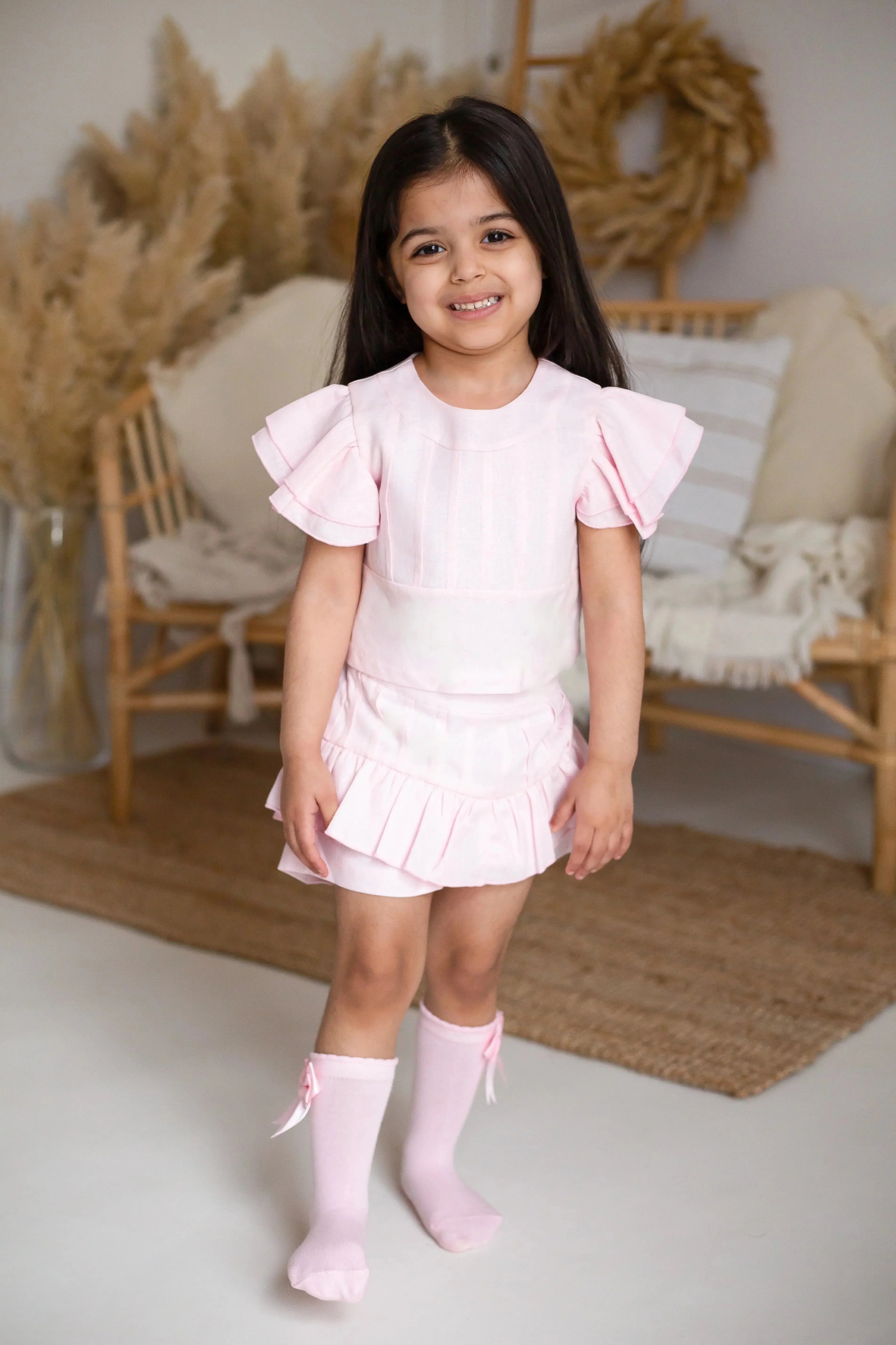 Smiling little girl in light pink ruffle dress and matching knee-high socks in cozy living room