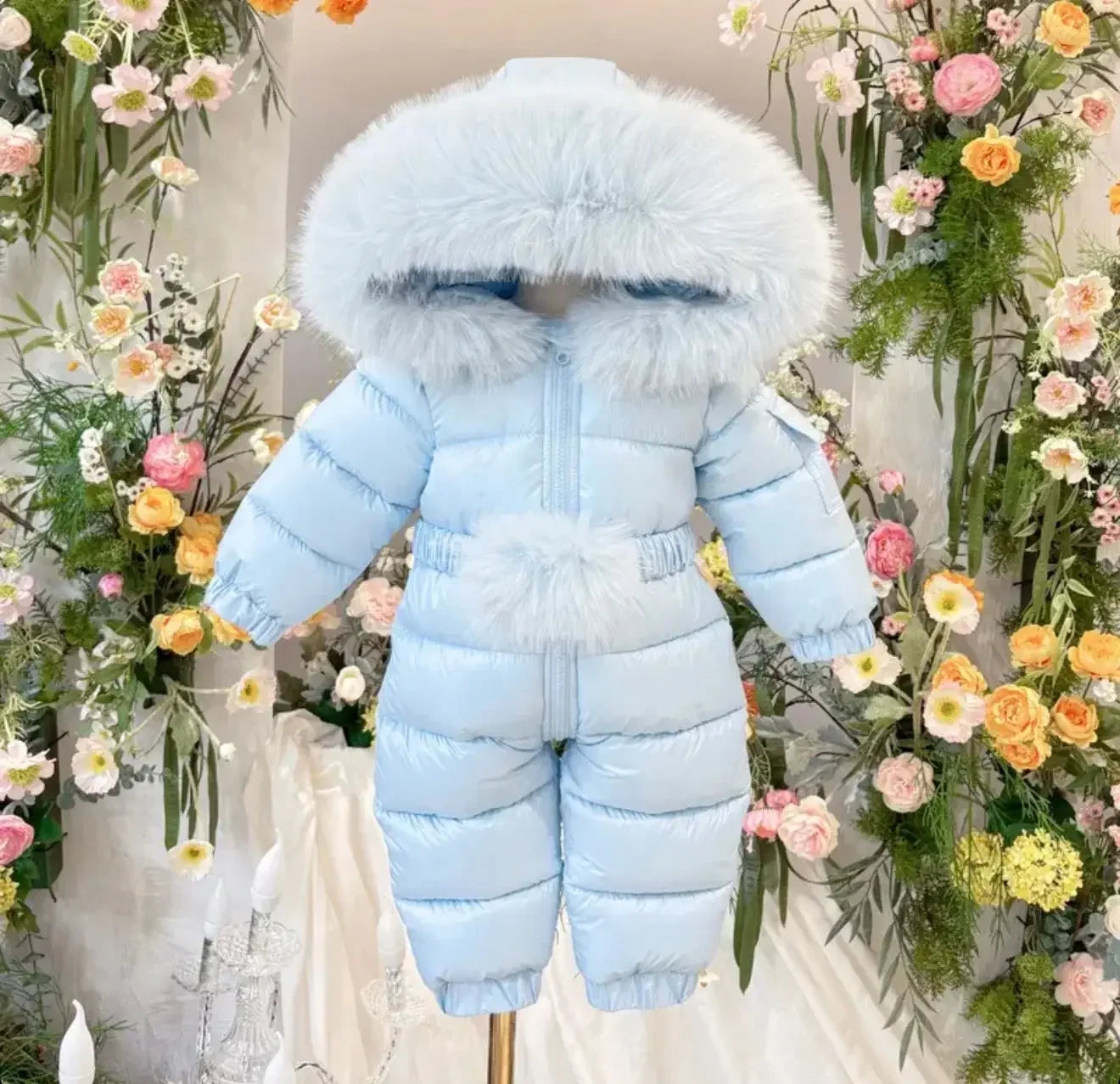 Light blue padded baby snowsuit with fur-trimmed hood displayed among colorful flowers
