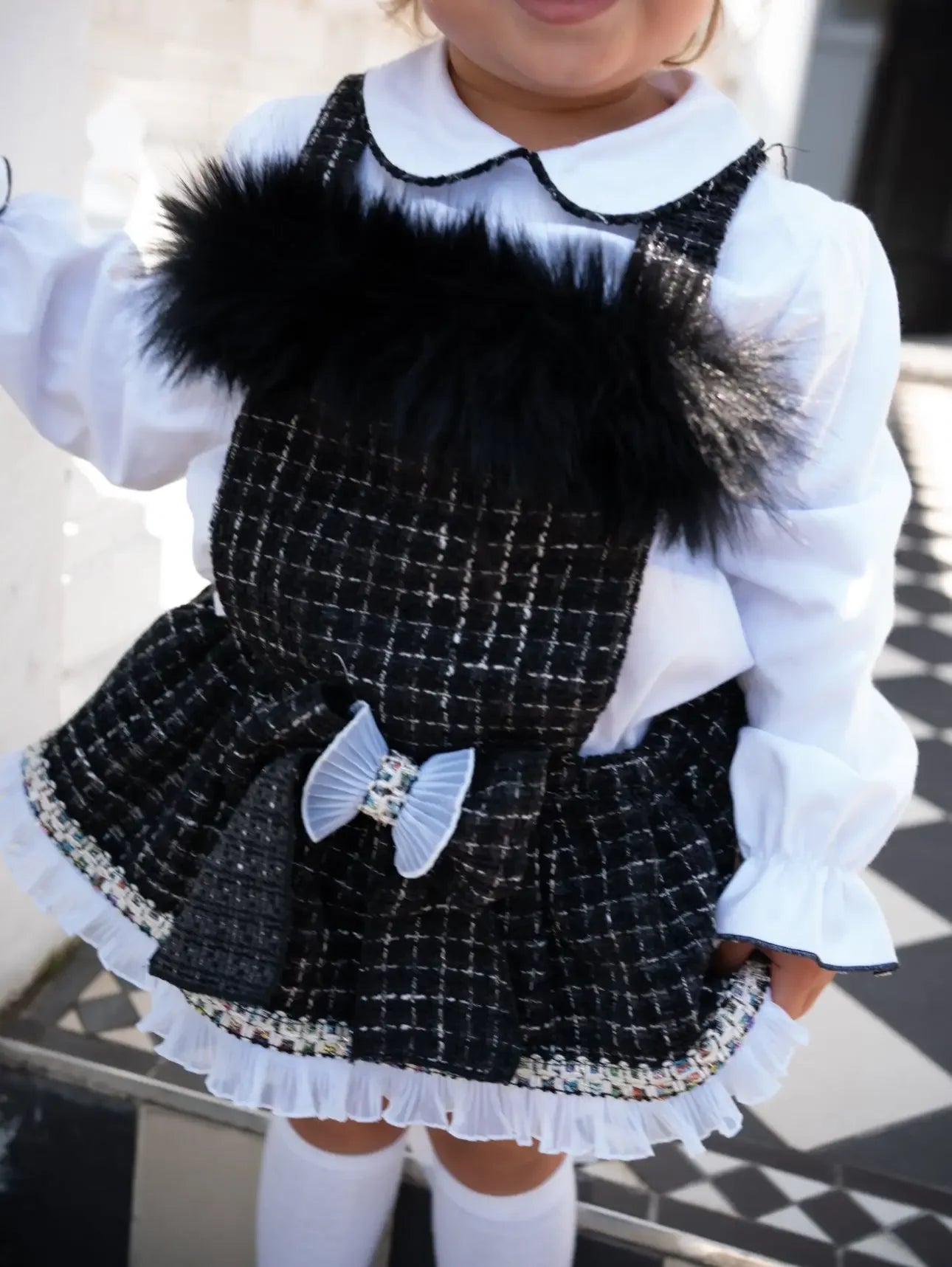 Toddler wearing black and white checkered dress with black fur trim, white blouse, and knee-high socks