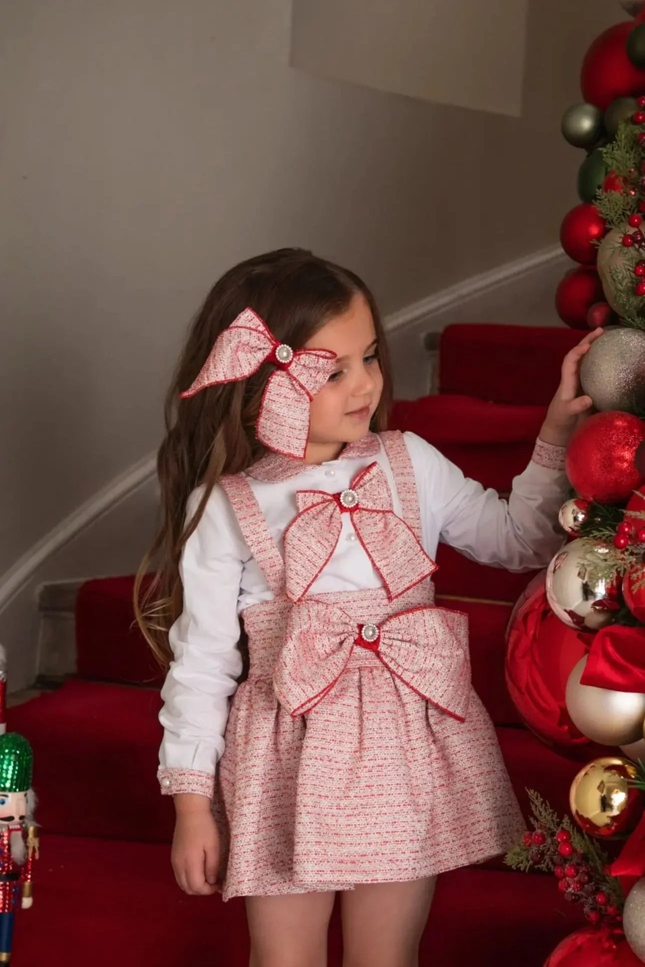 Young girl in festive pink bow dress and matching hair bow standing by Christmas decorations