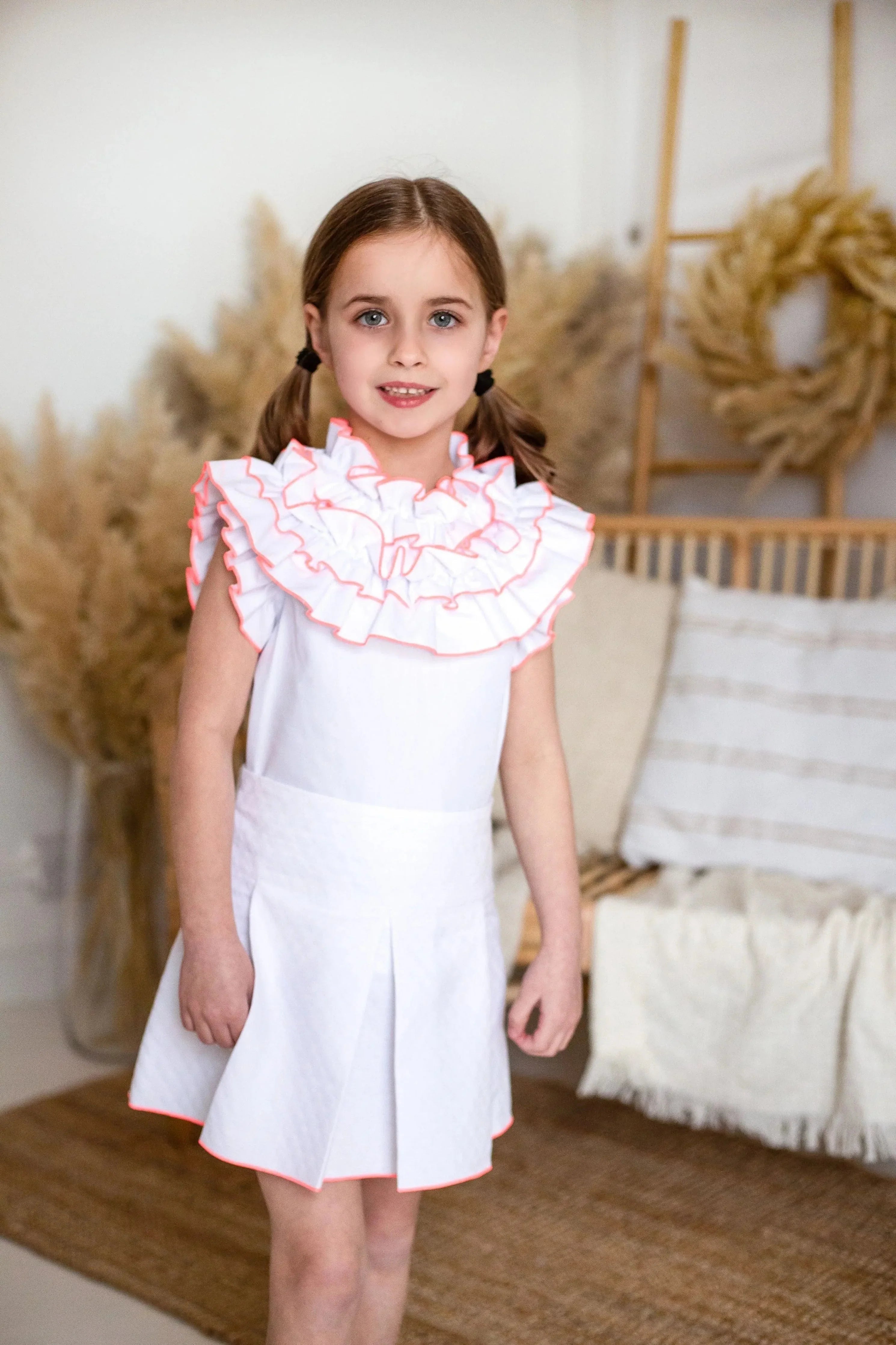 Young girl in white dress with neon orange ruffle details posing in cozy modern room