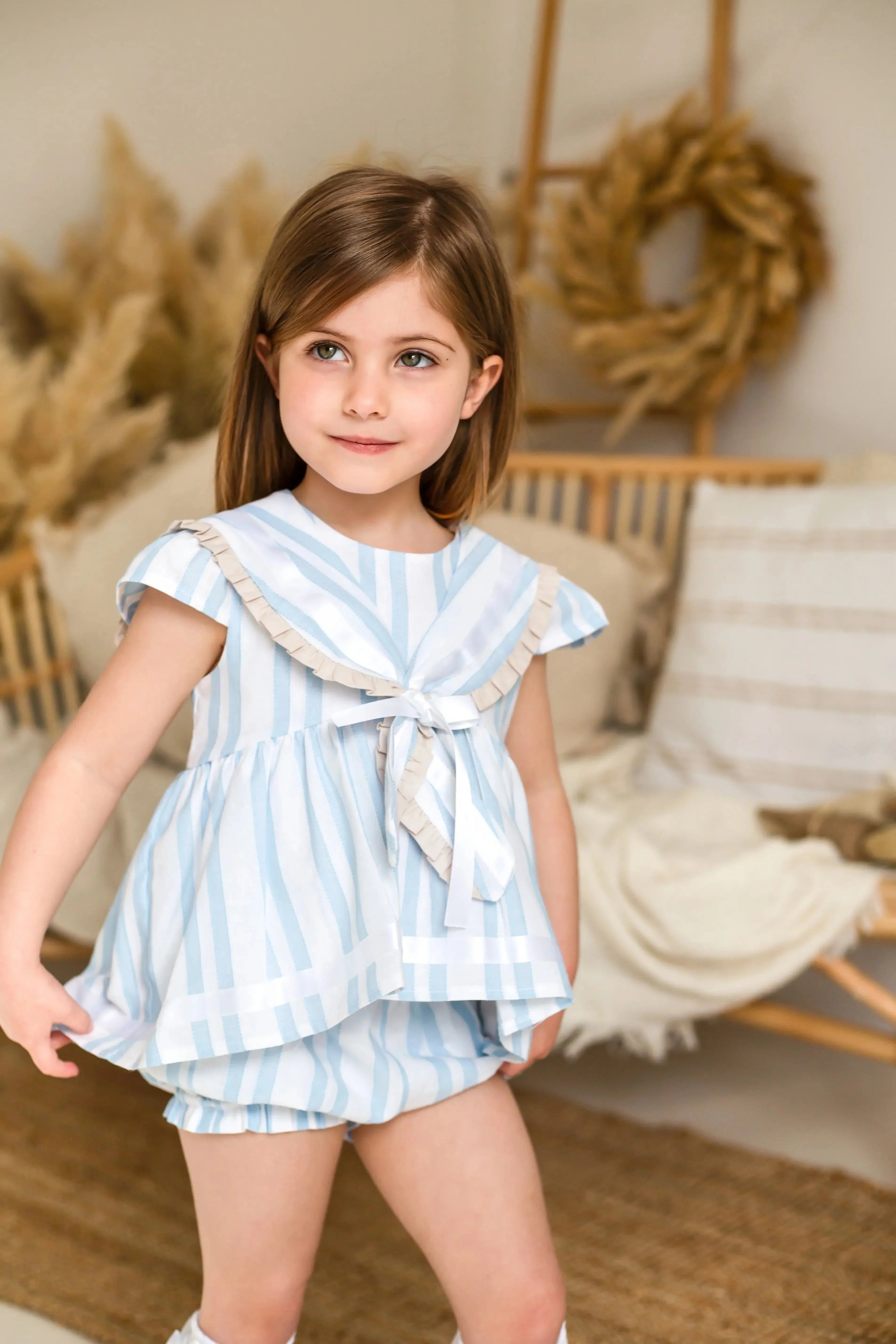 Young girl wearing exclusive baby blue linen stripe sailor short set in cozy neutral living room