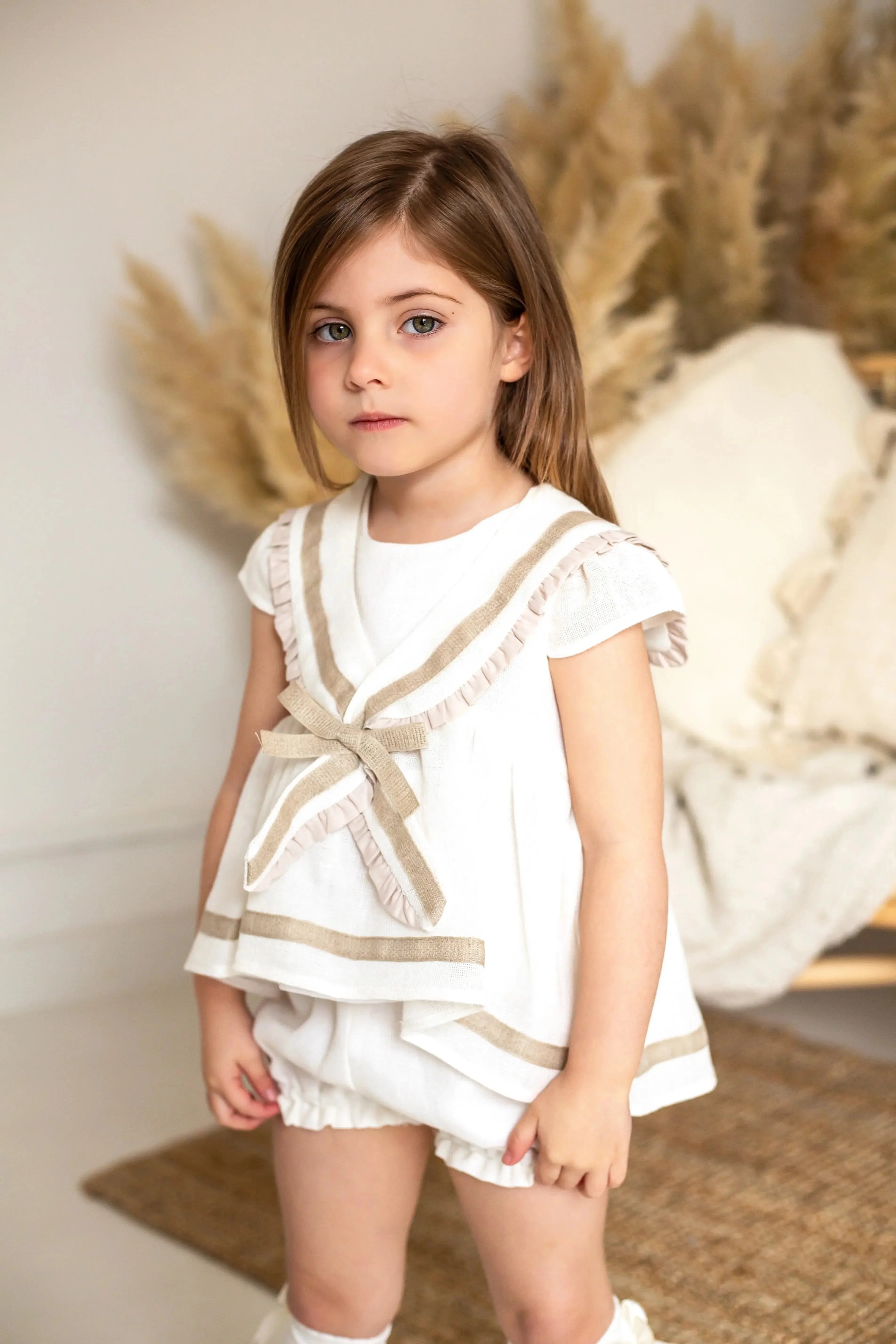 Young girl wearing cream and camel sailor short set in a cozy indoor setting with pampas grass