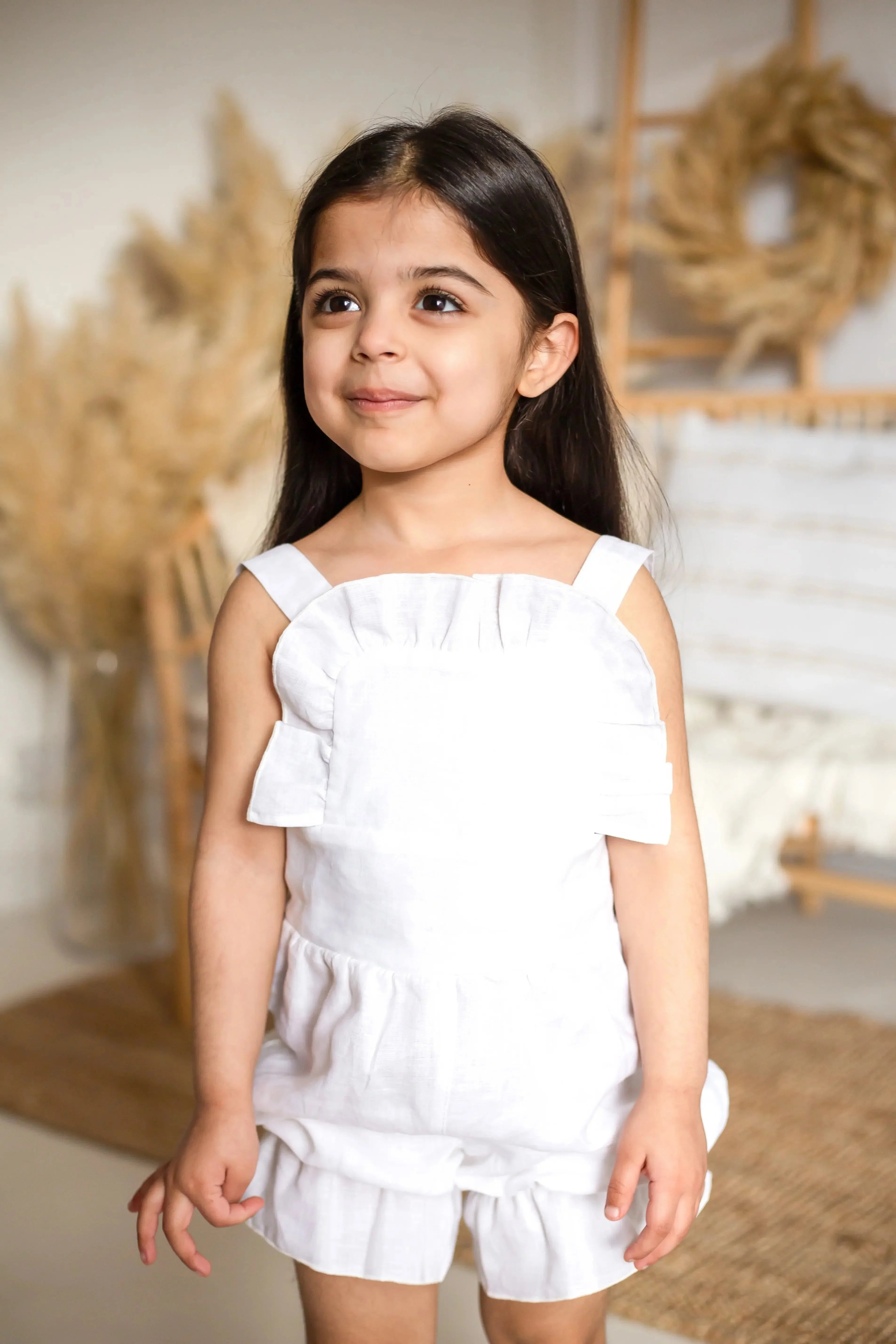 Smiling young girl in white summer romper with ruffles standing indoors with neutral décor
