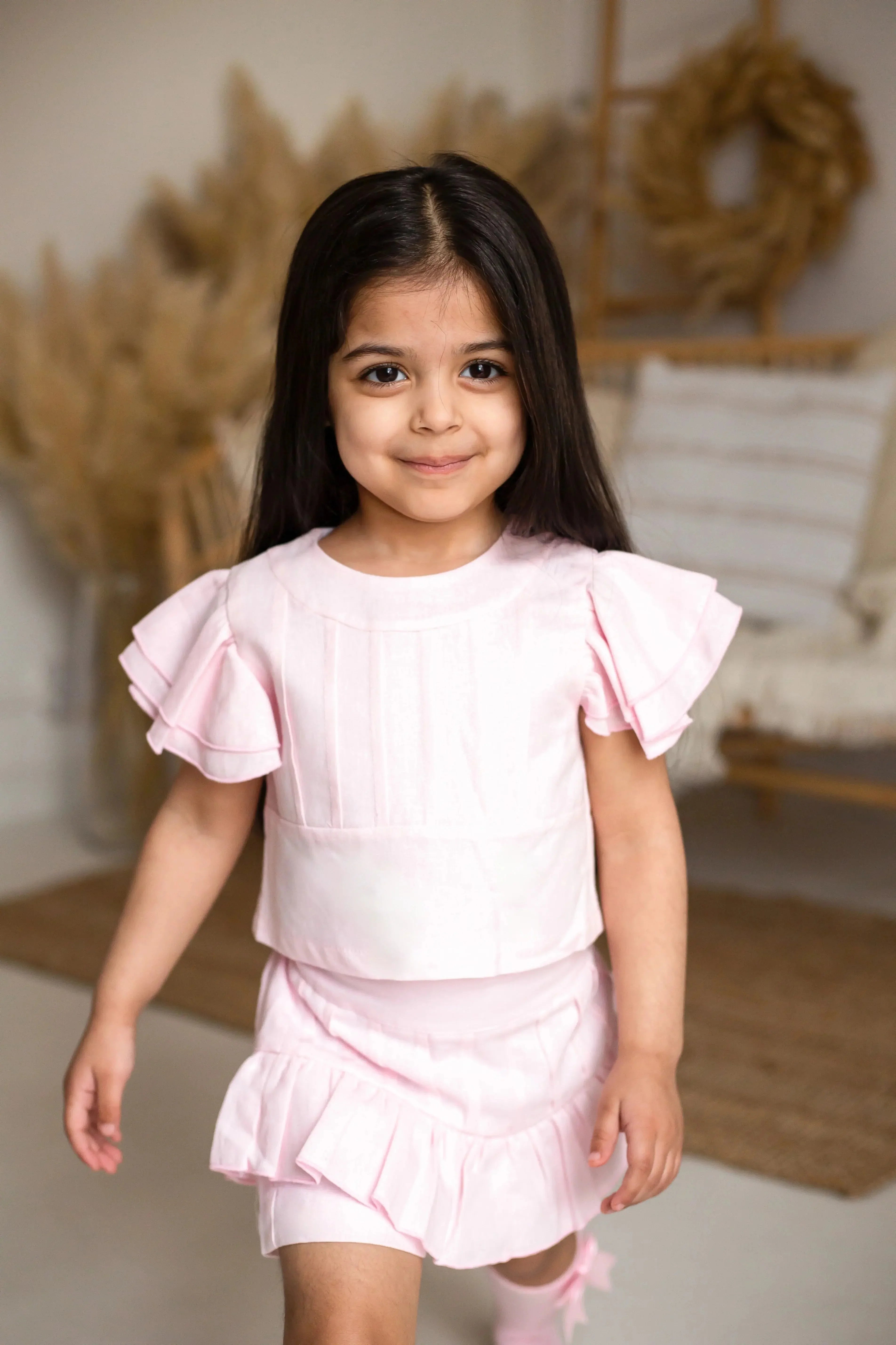 Smiling young girl in pink ruffle dress walking indoors with neutral decor background