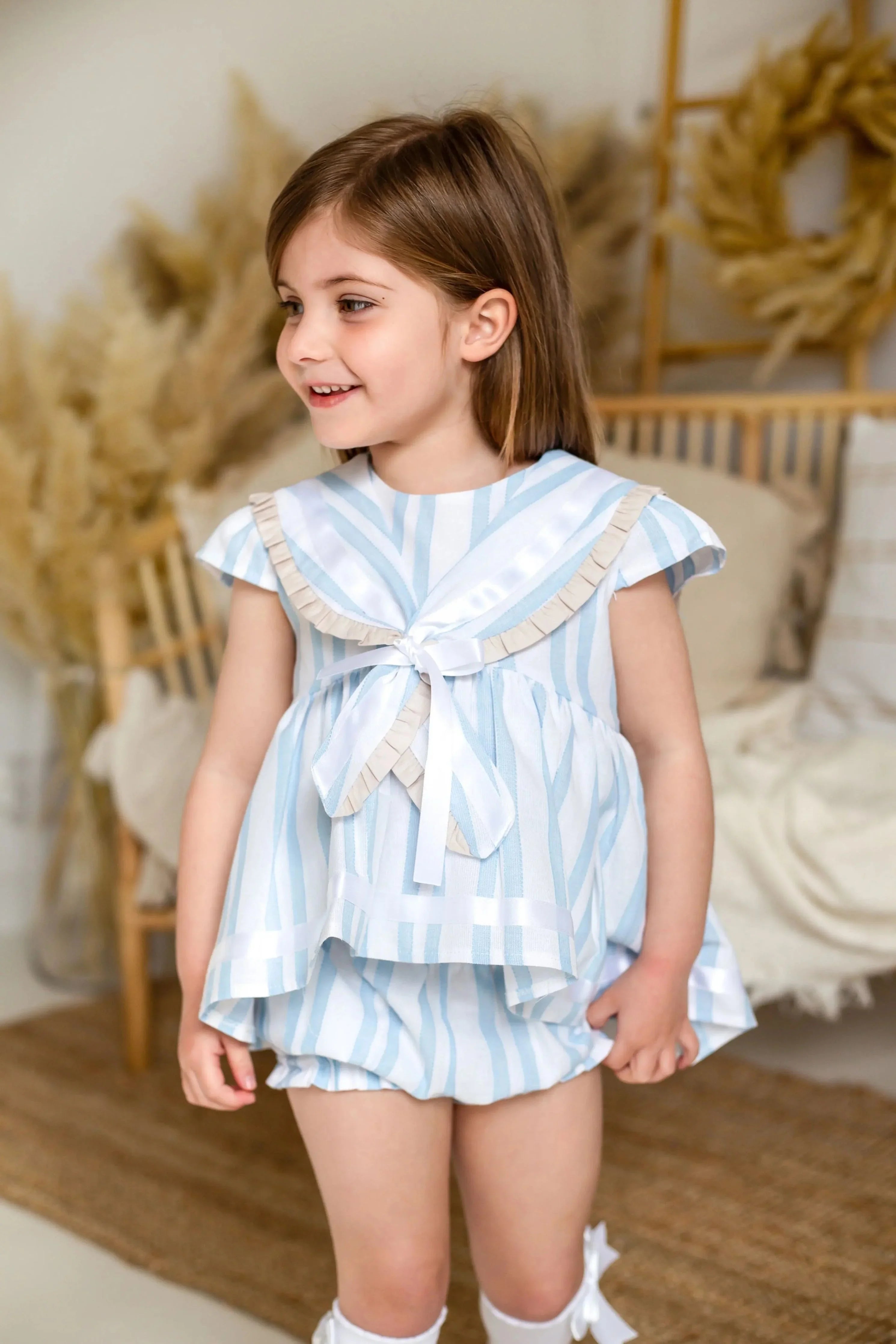 Little girl wearing exclusive baby blue linen stripe sailor short set in cozy home setting