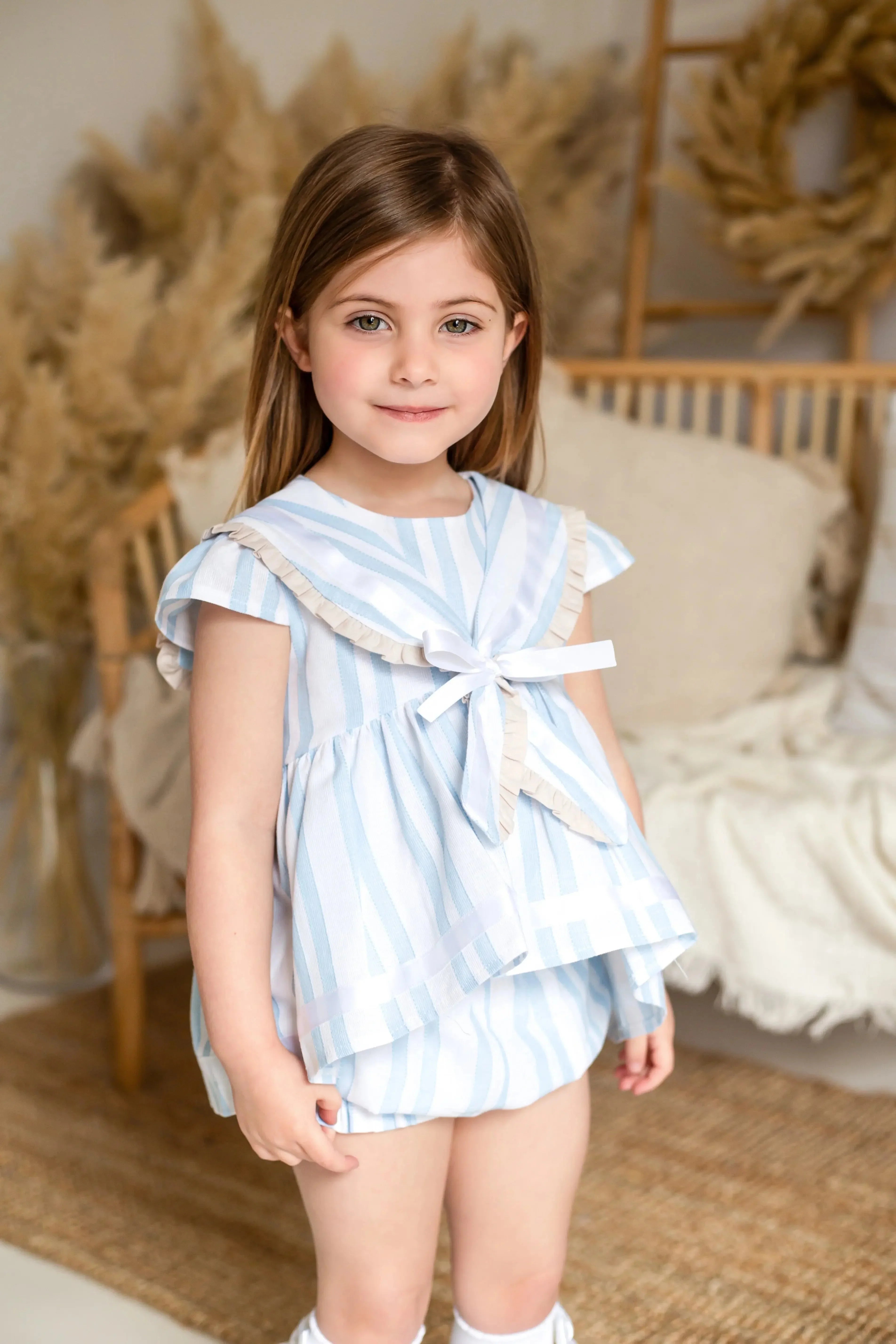Young girl wearing exclusive baby blue striped linen sailor top and shorts in cozy neutral indoor setting