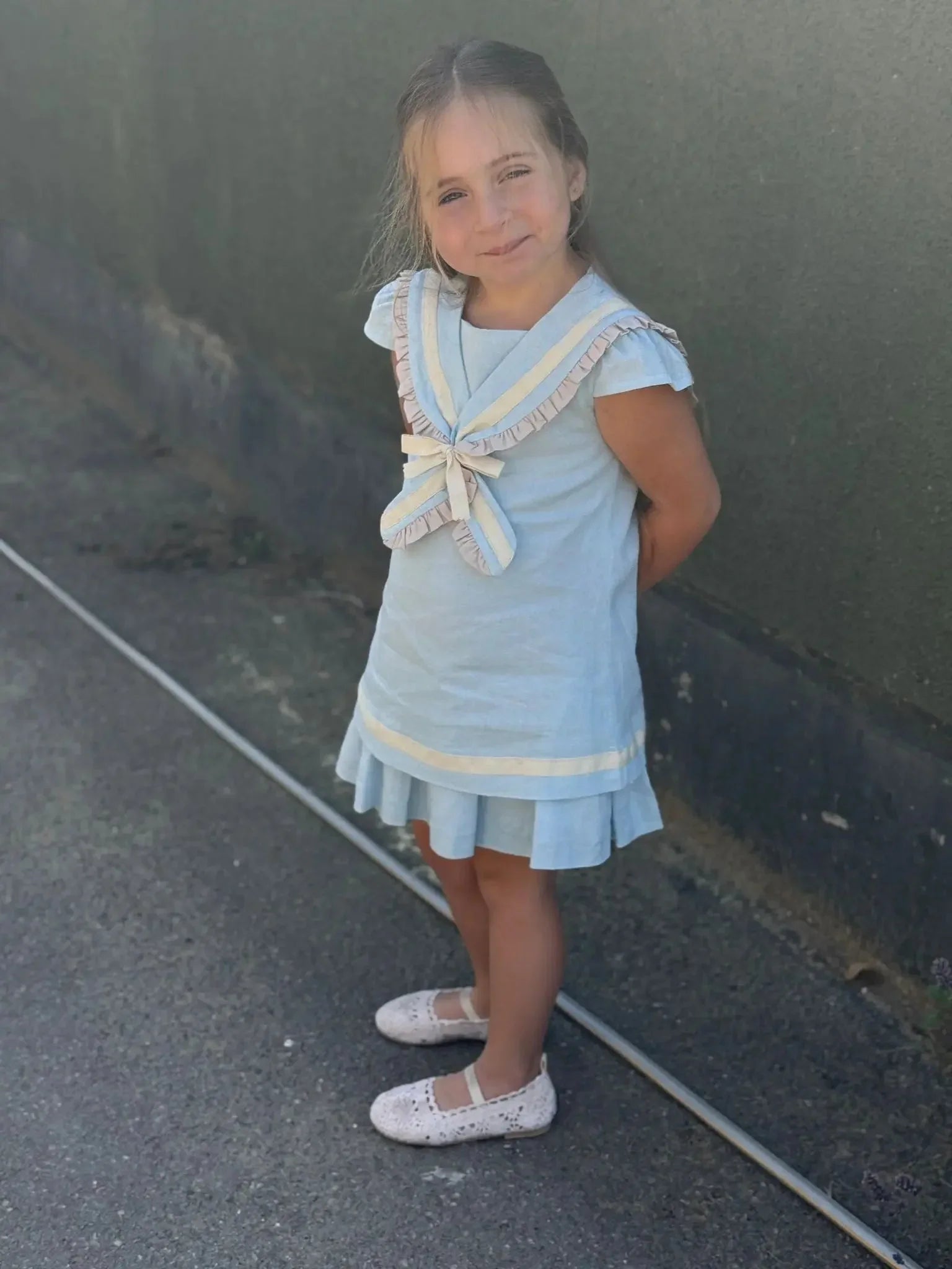 Young girl wearing a baby blue linen sailor A-line dress with beige trim standing outdoors