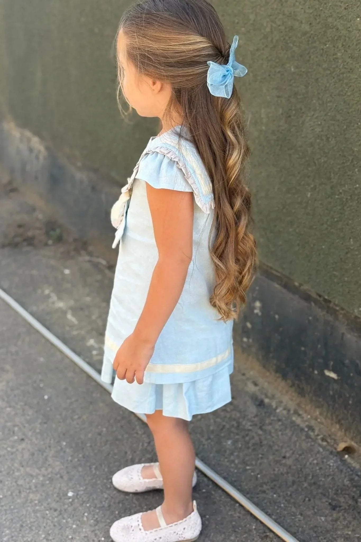 Young girl in baby blue linen sailor dress with ruffles and blue bow in long curly hair
