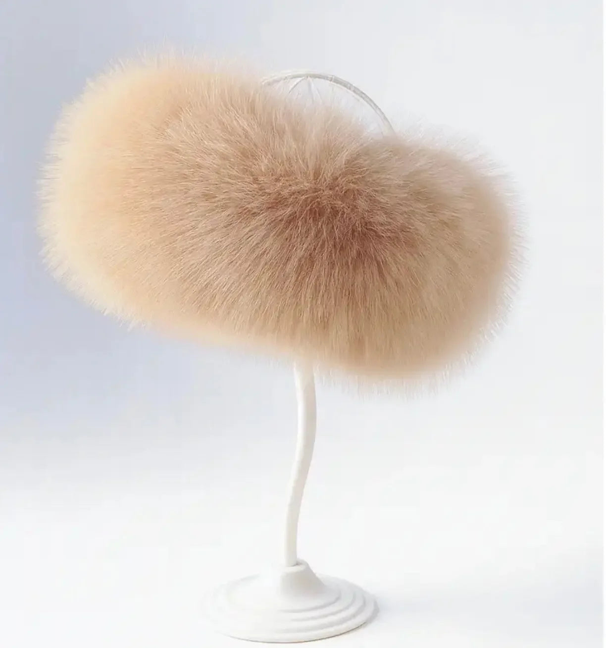 Soft beige fluffy fur muff displayed on a white minimalist stand against a light background