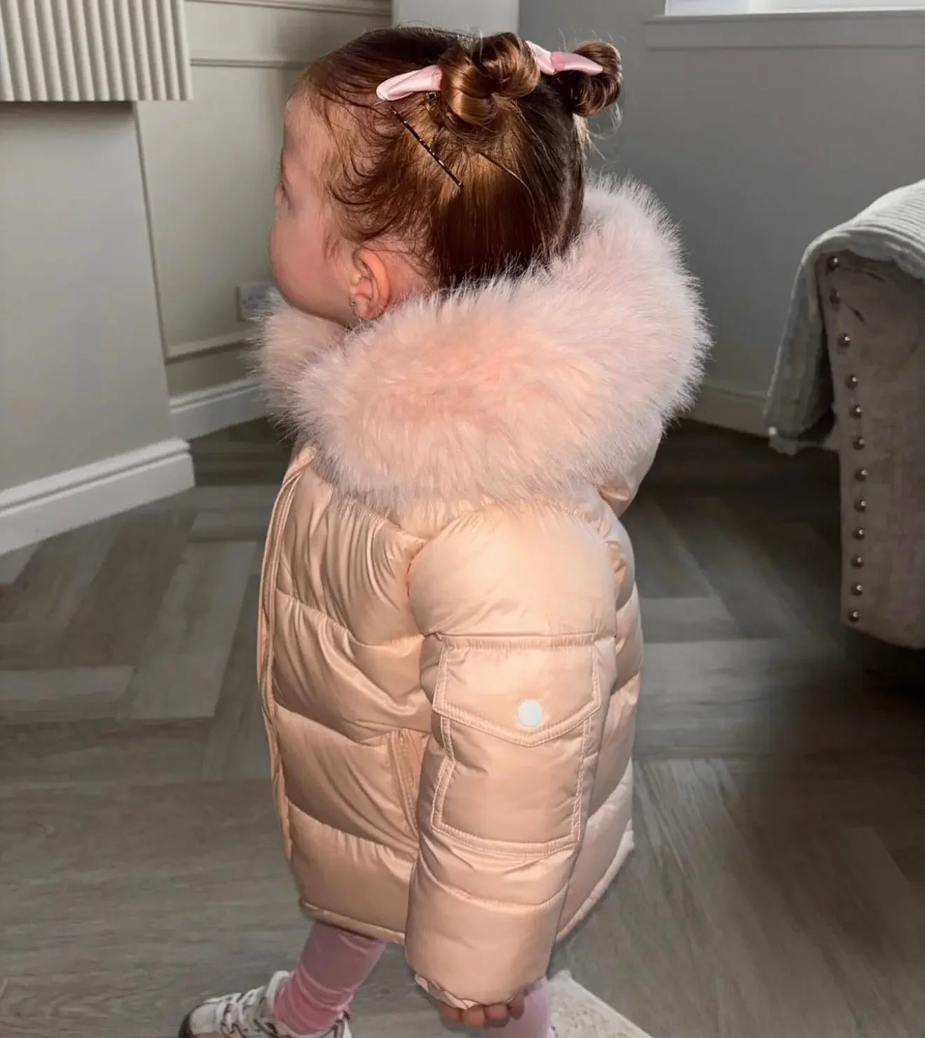 Toddler girl in pink puffer jacket with fur hood and pink hair clips indoors