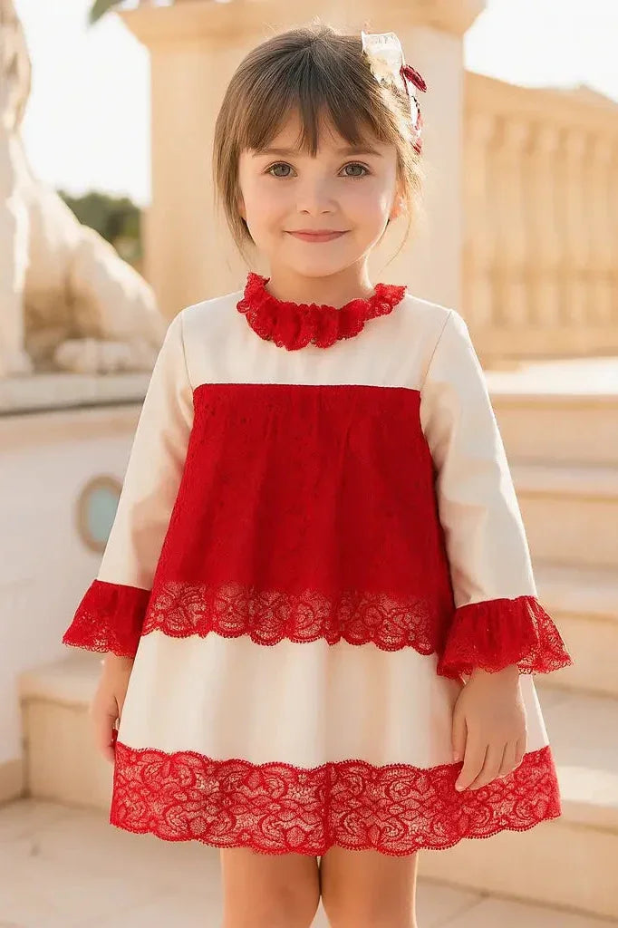 Smiling young girl wearing cream and red lace dress with ruffled collar, standing outdoors on stone steps