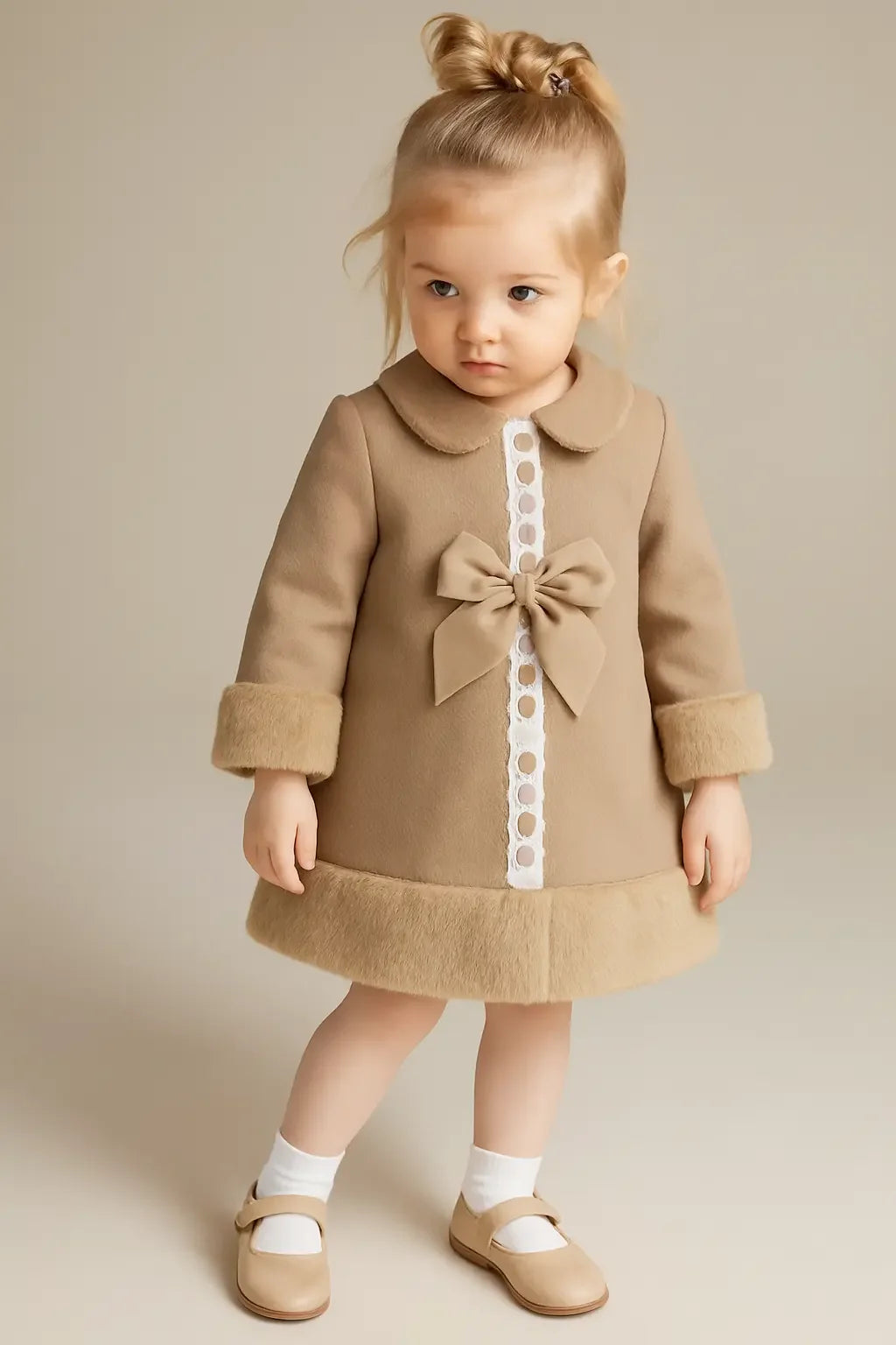 Toddler girl in beige coat with bow and fur trim, white socks, beige Mary Jane shoes, neutral background