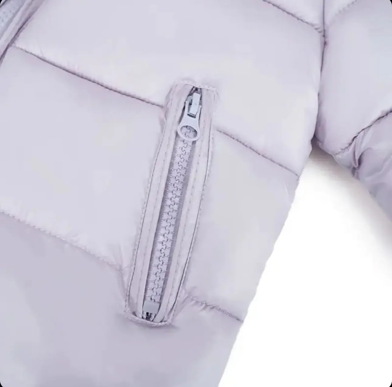 Close-up of light gray quilted jacket sleeve with silver zipper pocket detail