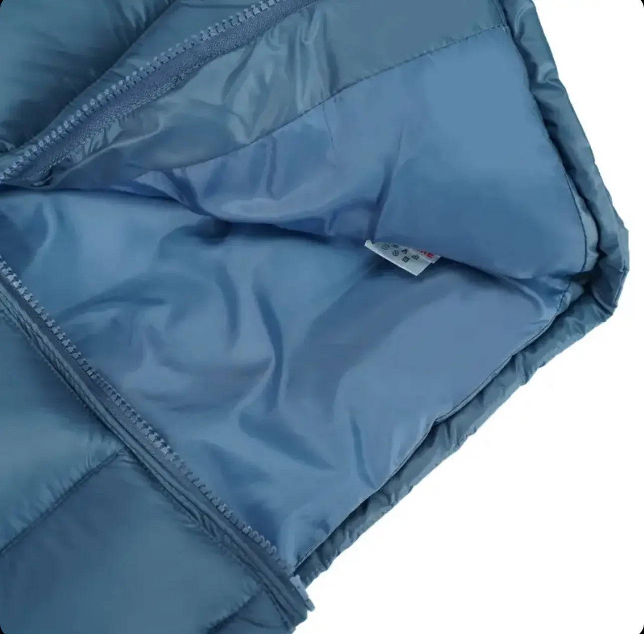 Close-up of light blue quilted jacket with open zipper showing smooth inner lining and fabric tag