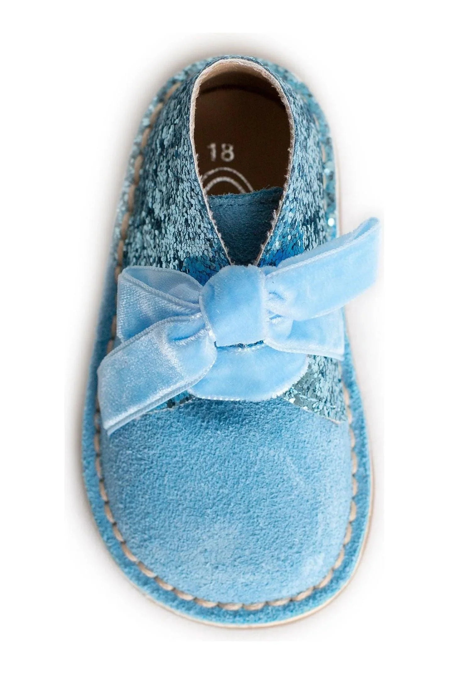 Blue glitter toddler shoe with suede toe and velvet bow closure on white background