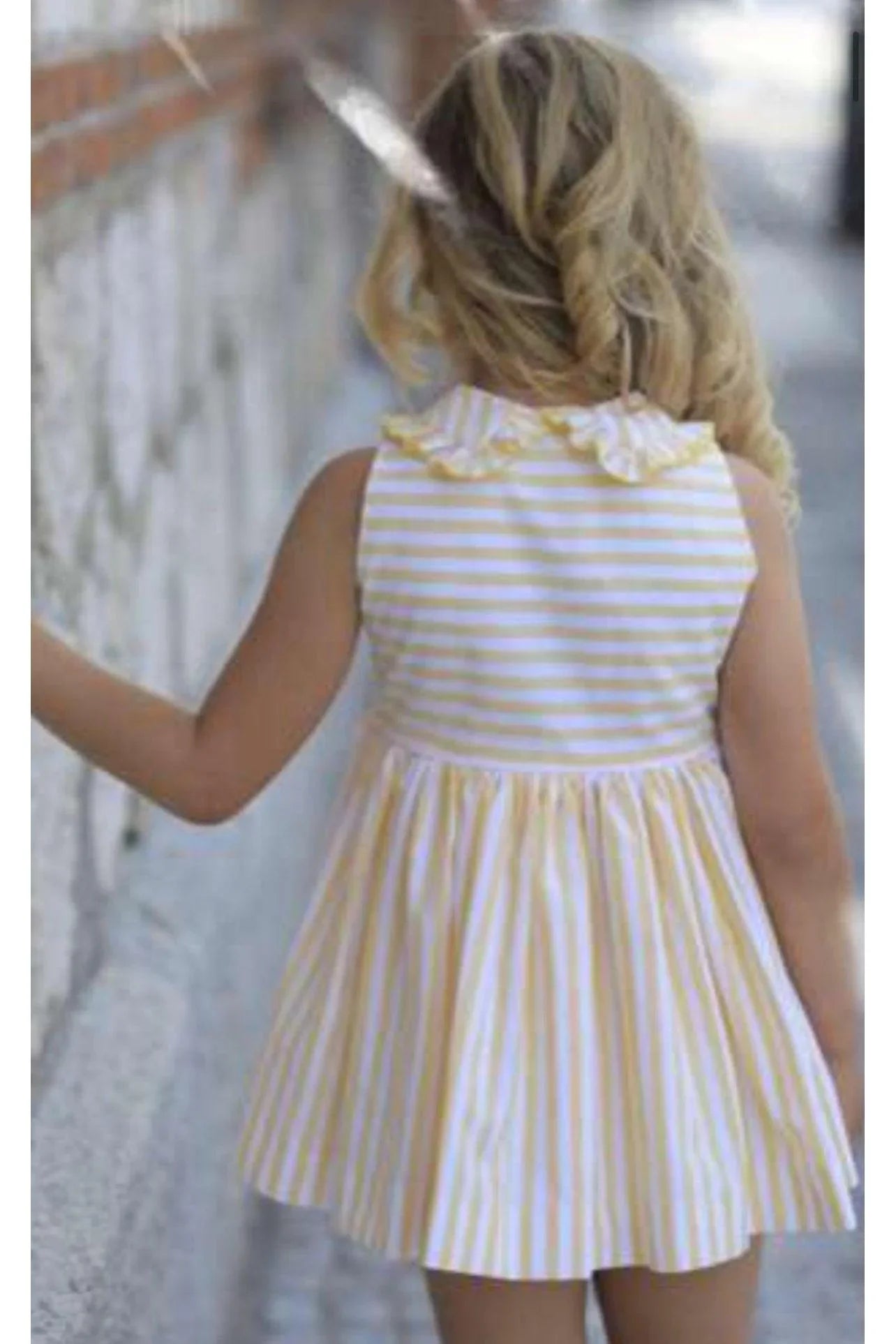 Child wearing yellow and white striped summer dress with ruffle collar walking outdoors