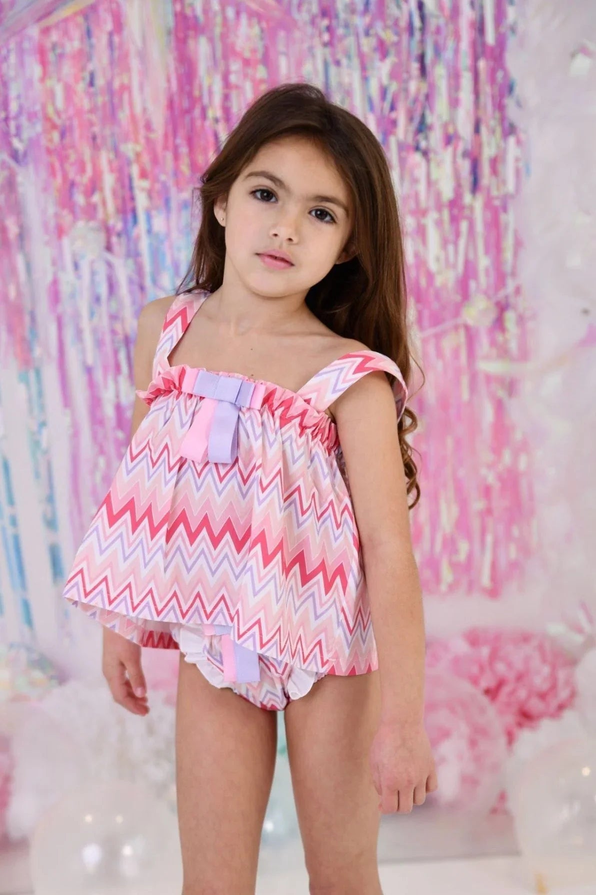 young girl wearing pink zigzag patterned bathing suit top and matching bottoms against colorful pastel backdrop