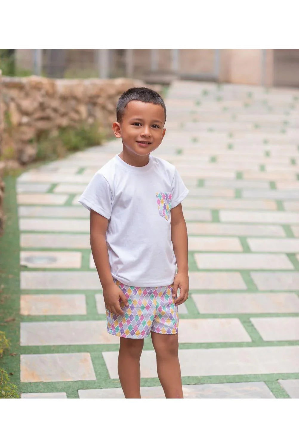 Young boy wearing white t-shirt with colorful diamond pocket and matching shorts on outdoor path