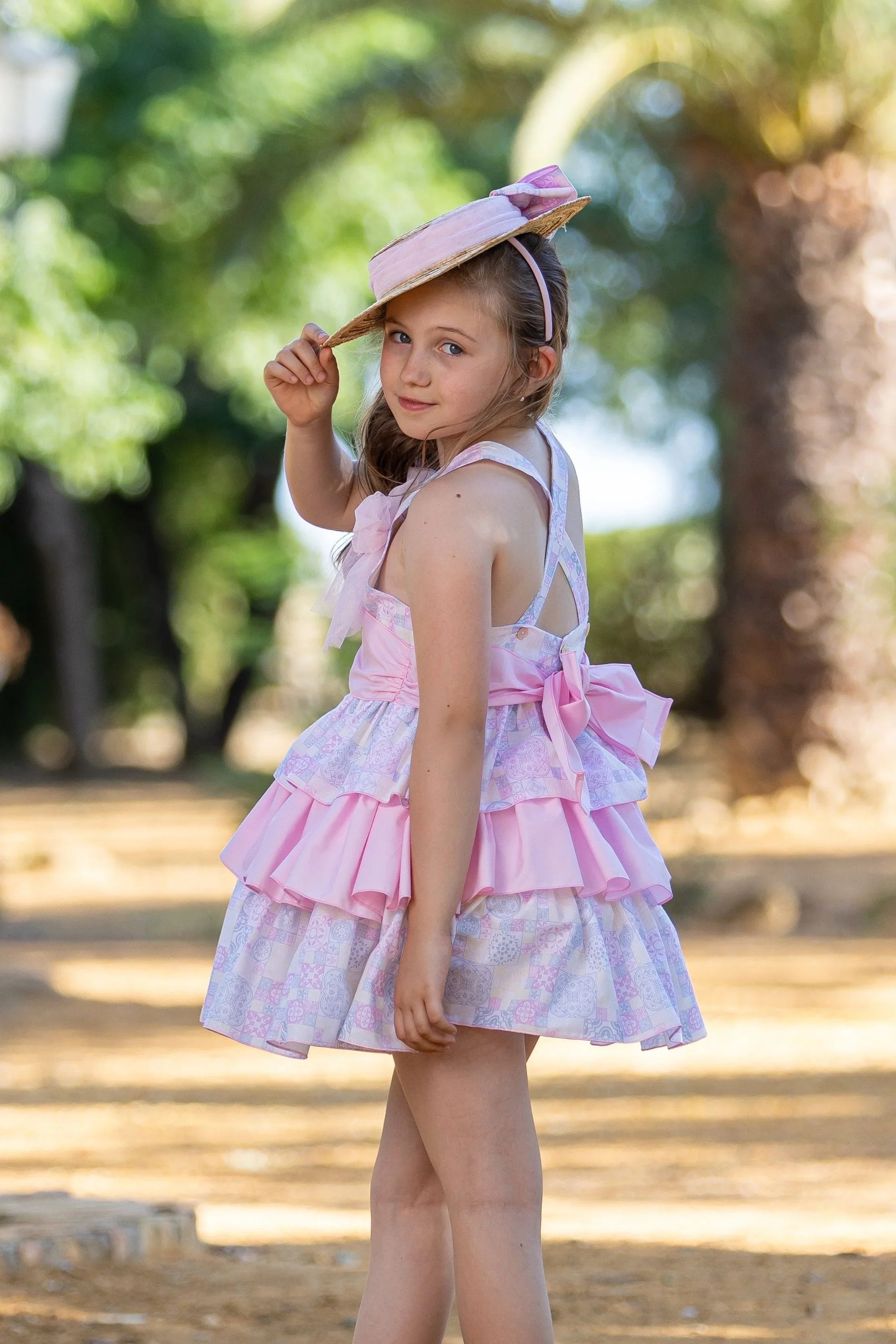 Young girl in a pink ruffled dress and straw hat with bow outdoors in sunny garden