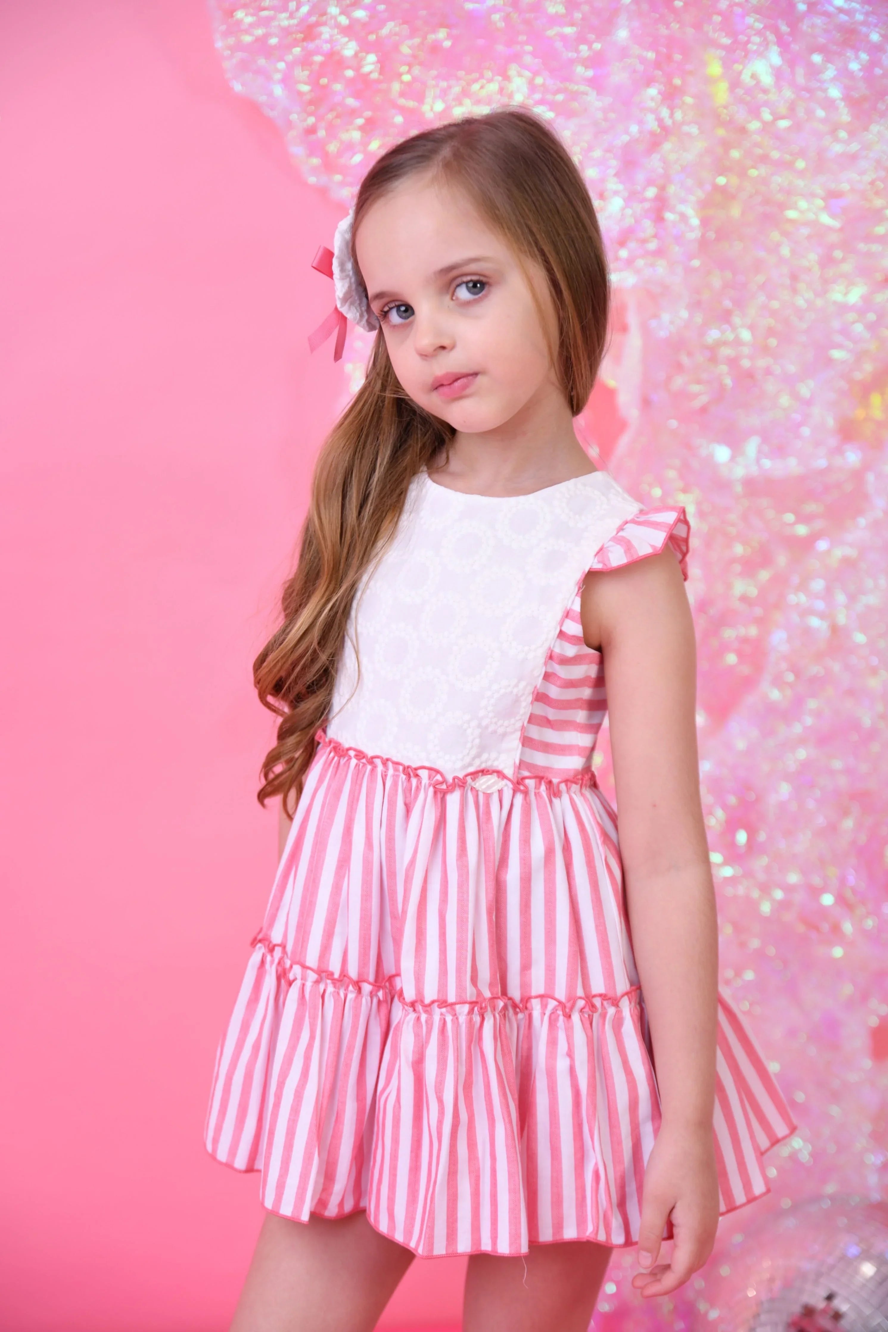 Young girl in pink and white striped summer dress with lace bodice on pink glittery background