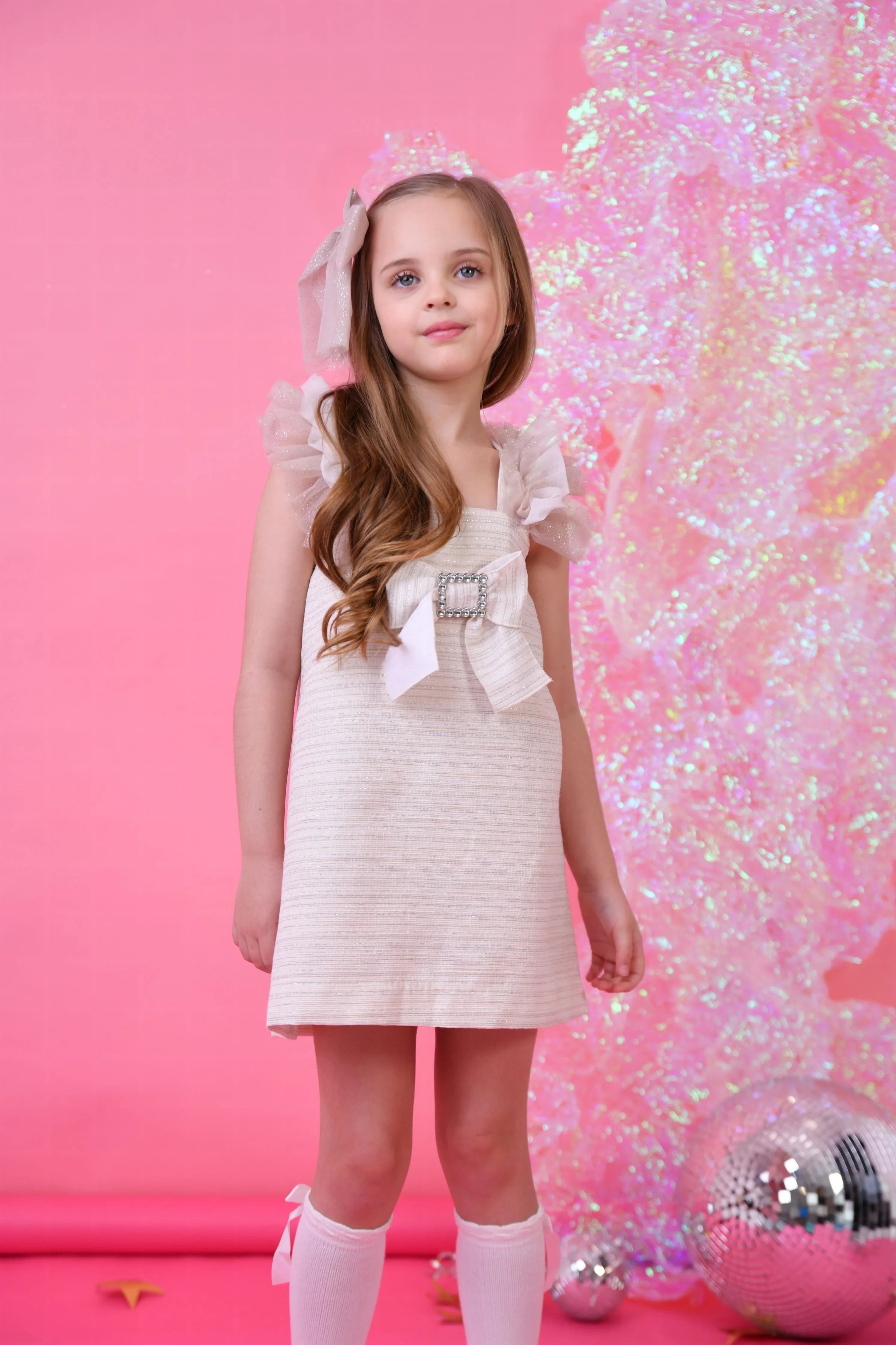 Young girl in biscuit glitter tulle dress with bow and ruffled sleeves against pink background