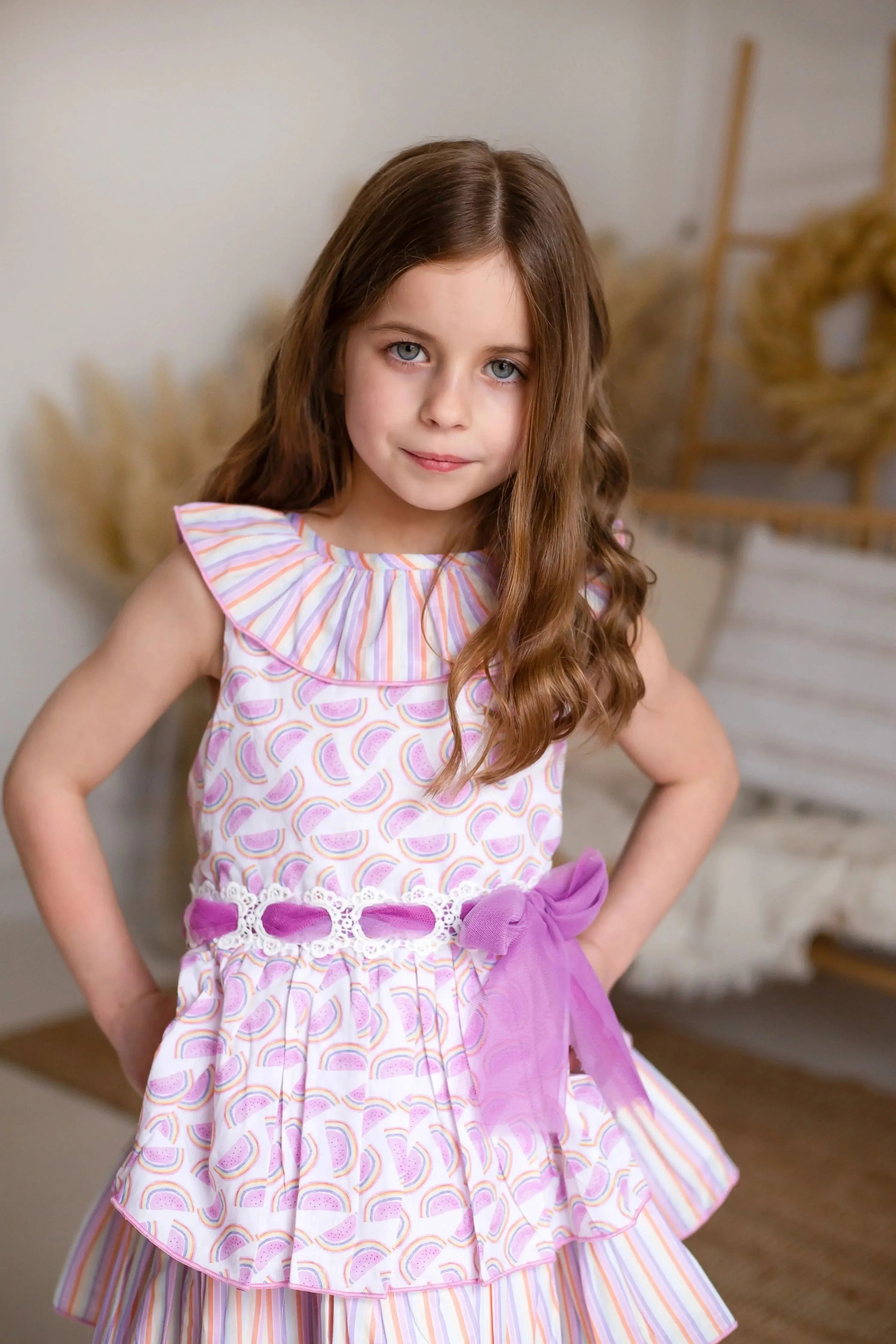 Girl wearing a pastel melon print dress with a ruffled collar and purple tulle belt indoors