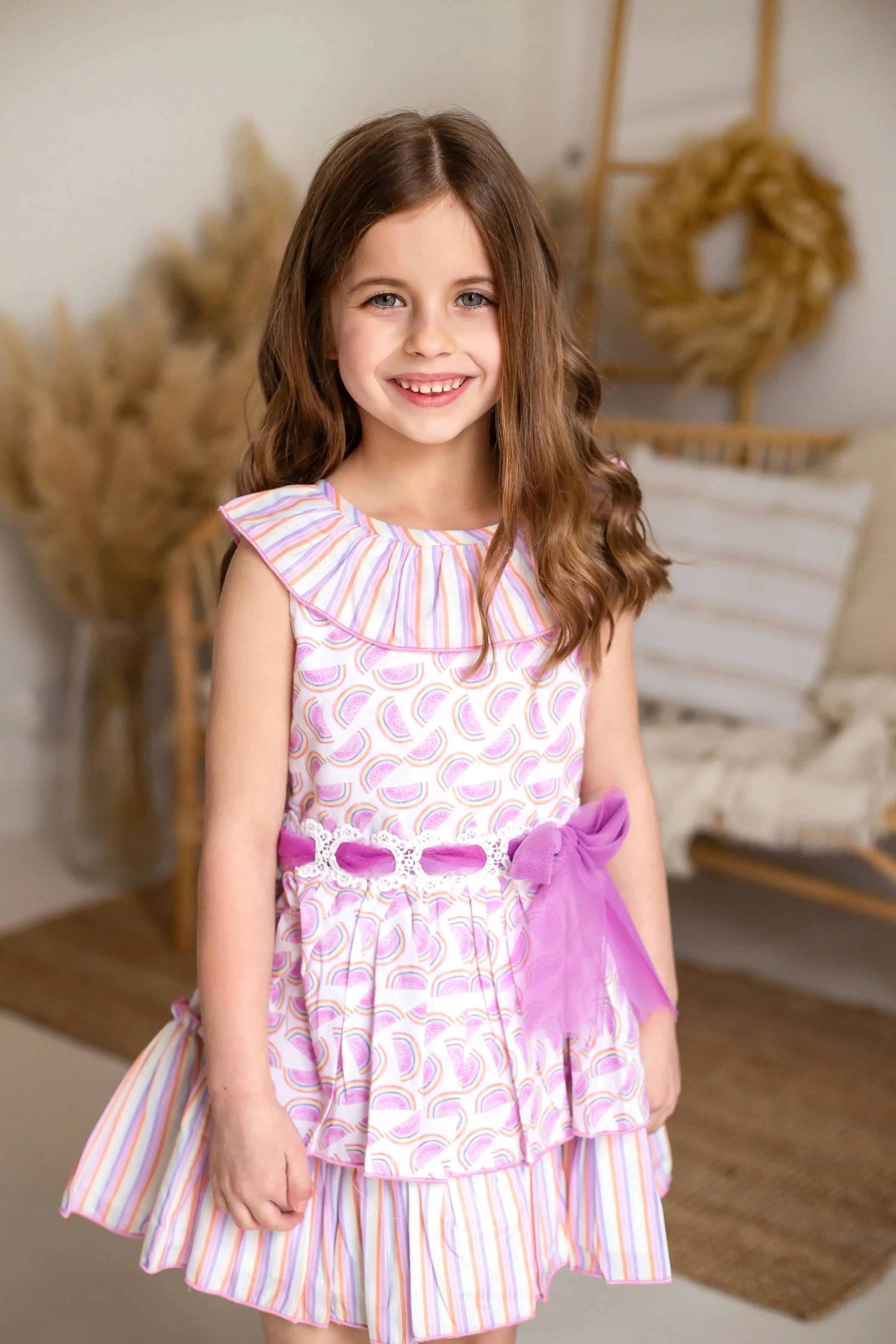 Smiling girl in watermelon print and striped dress with purple tulle bow in cozy indoor setting