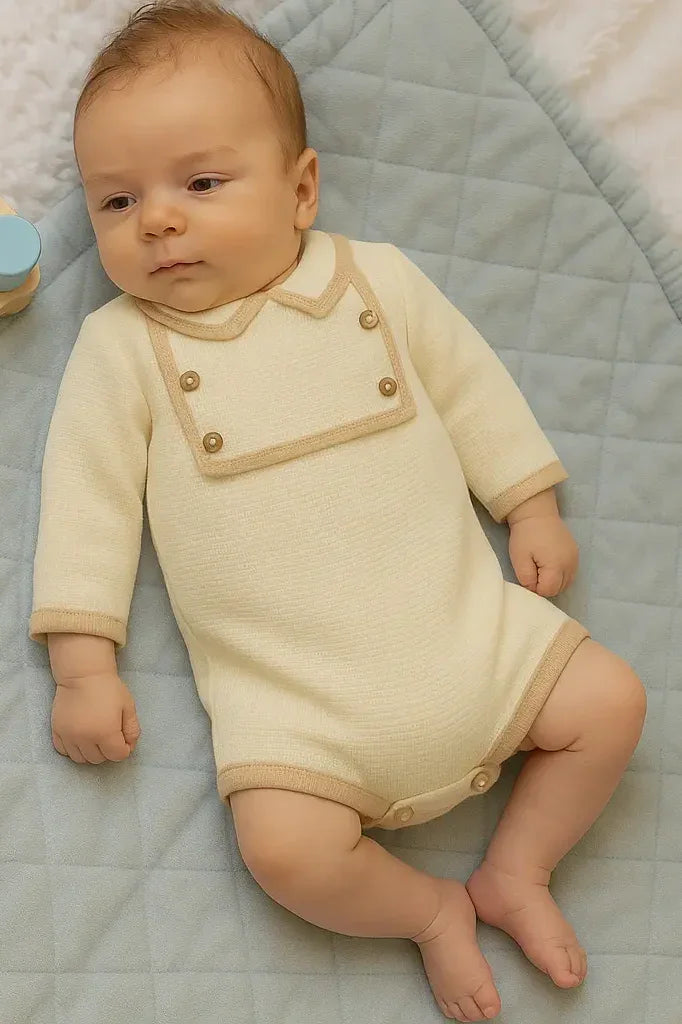 baby lying on quilted blue mat wearing cream romper with beige trim and wooden buttons