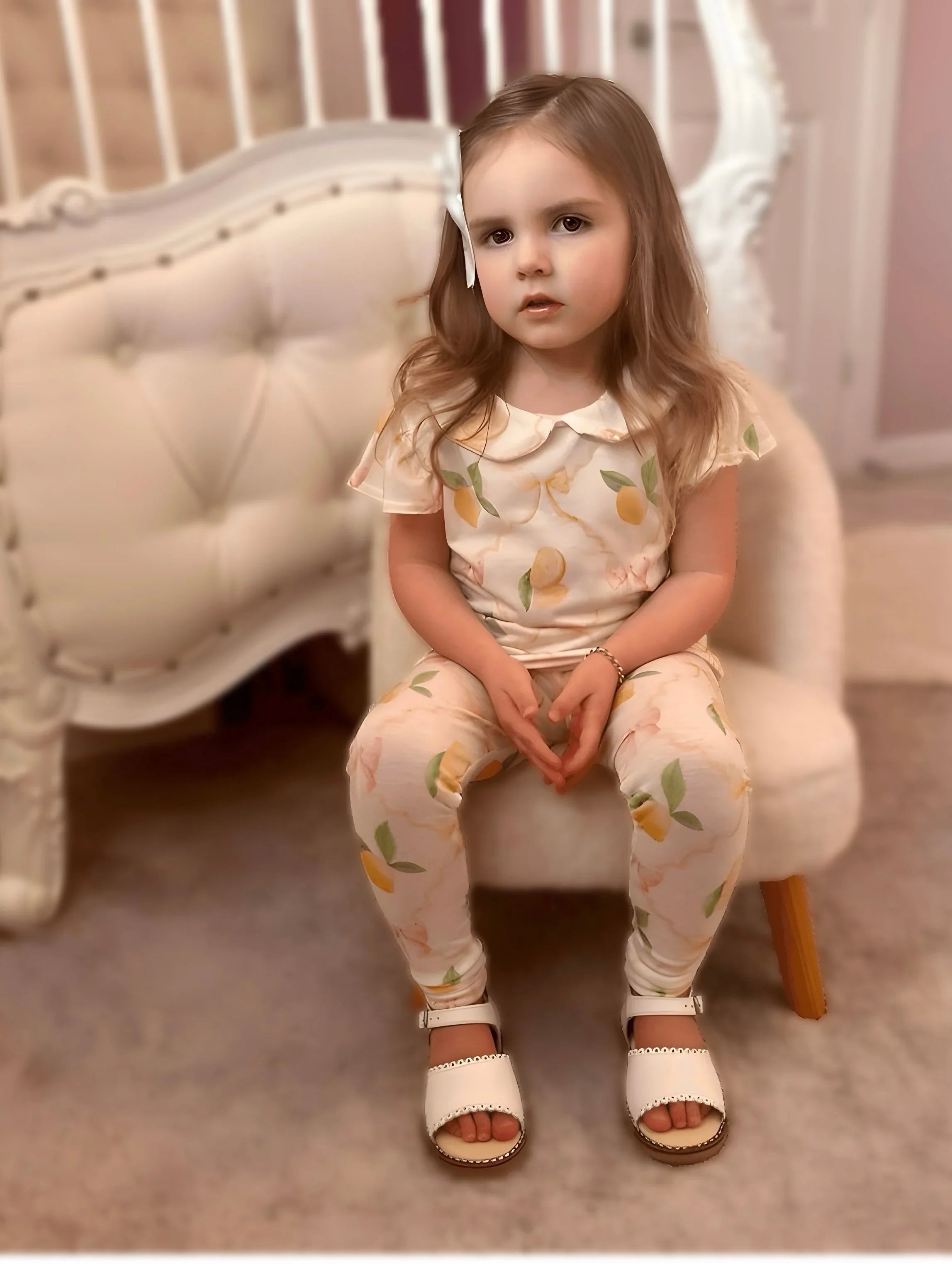Young girl sitting on beige chair wearing cream loungewear set with vintage lemon print and white sandals