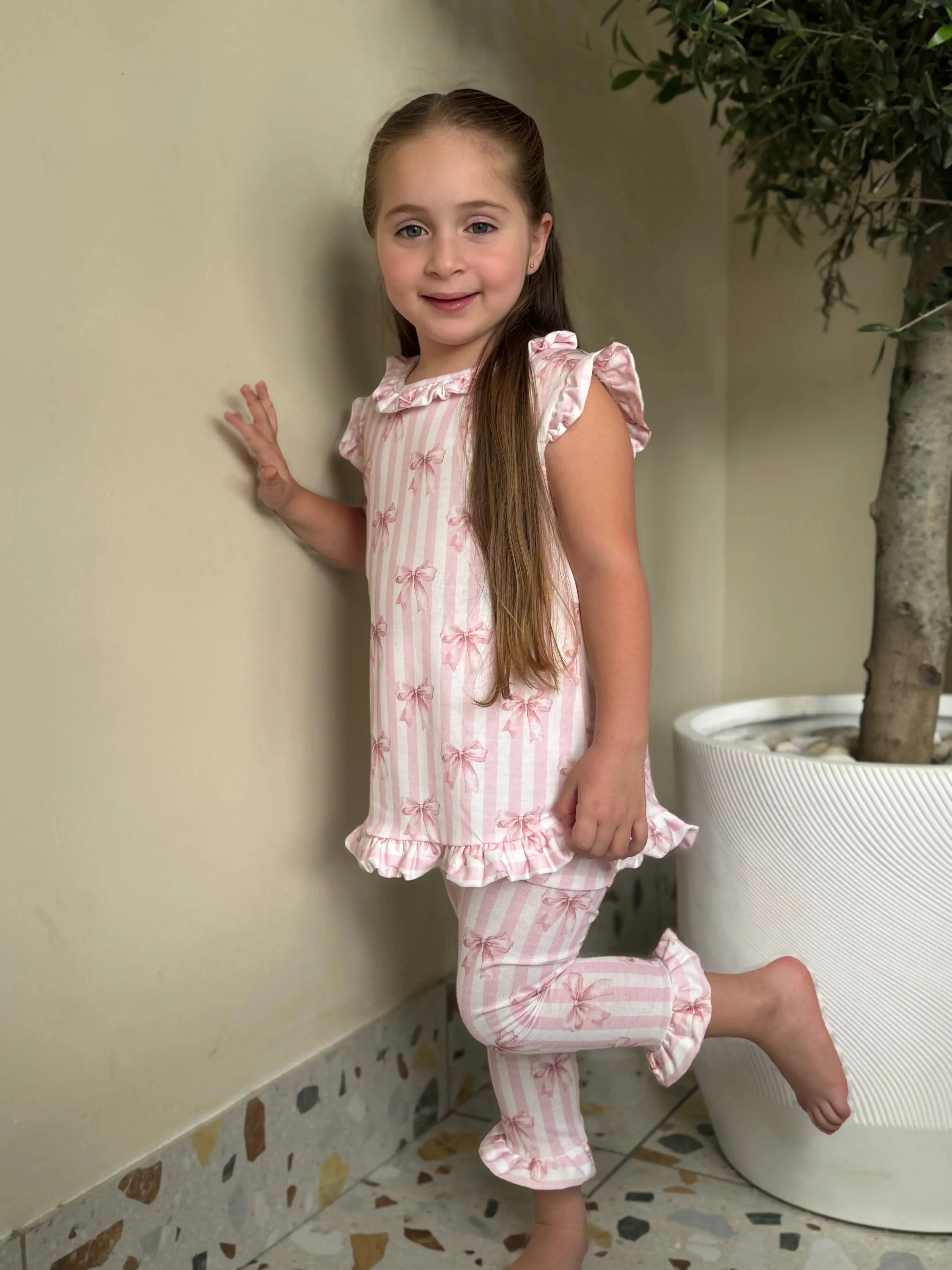 Young girl wearing pink and white striped ruffled pajama set with bow patterns indoors