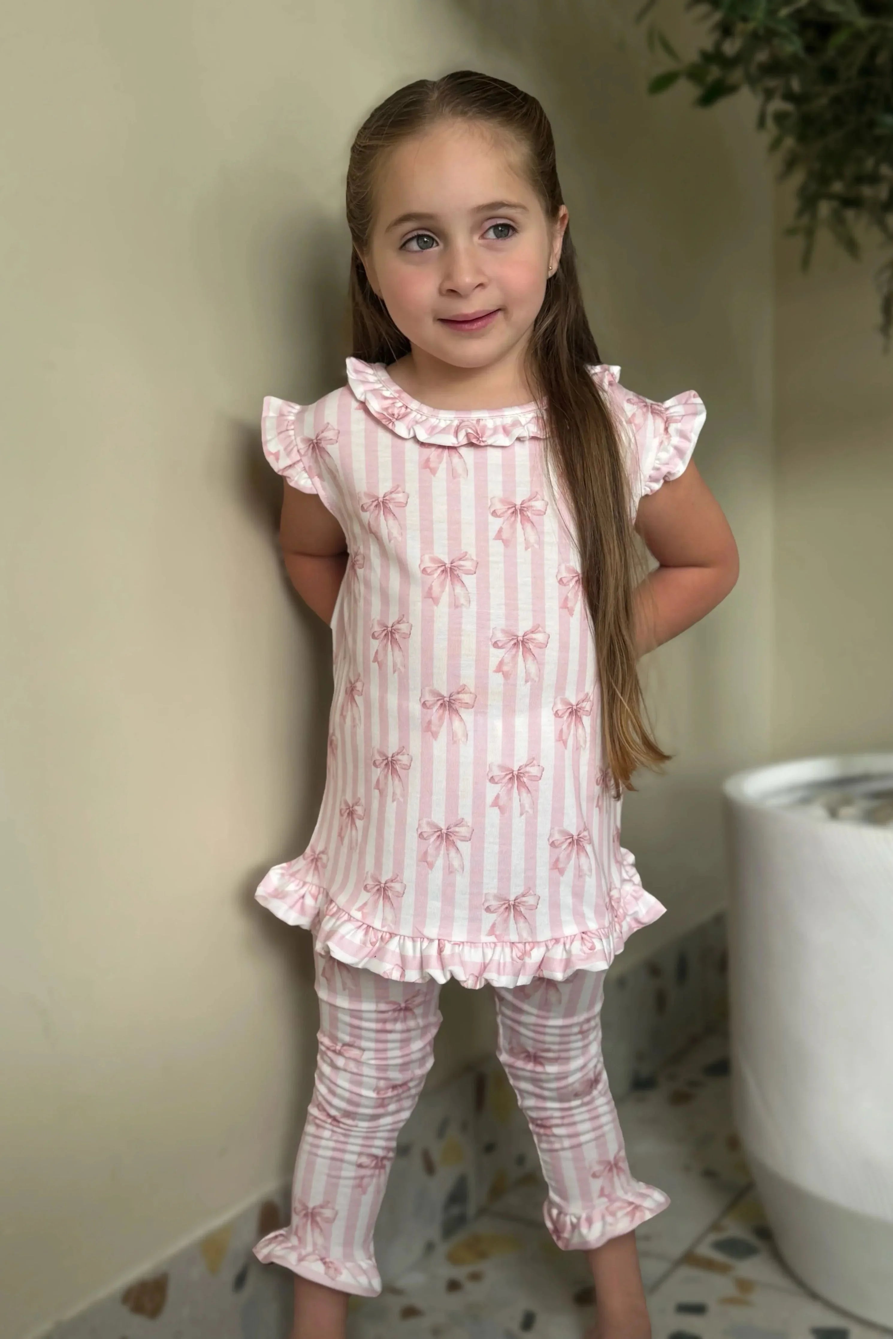 Young girl wearing pink and white striped loungewear set with bow print and ruffle details indoors