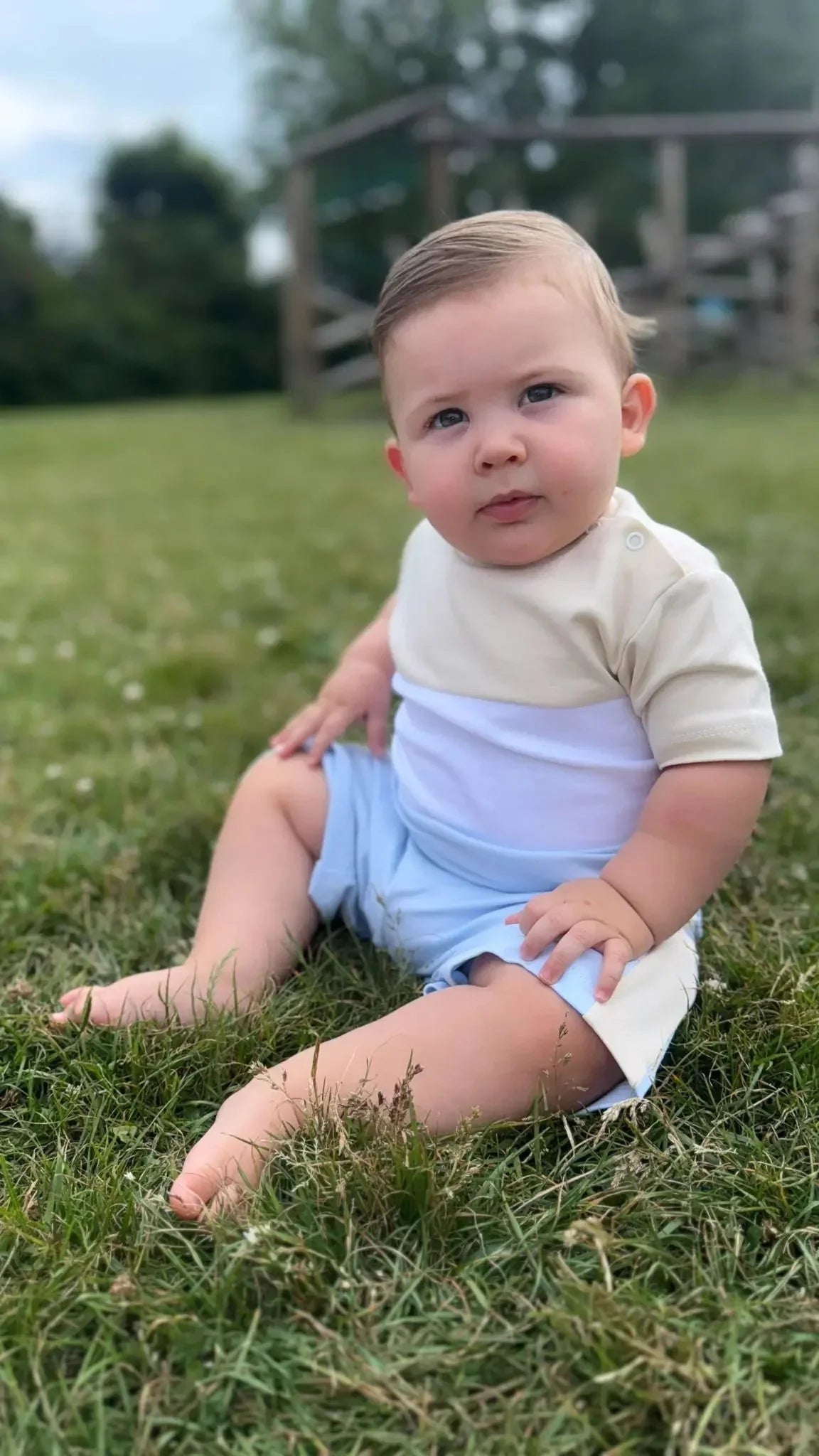 baby boy sitting on grass outdoors wearing beige and blue summer outfit
