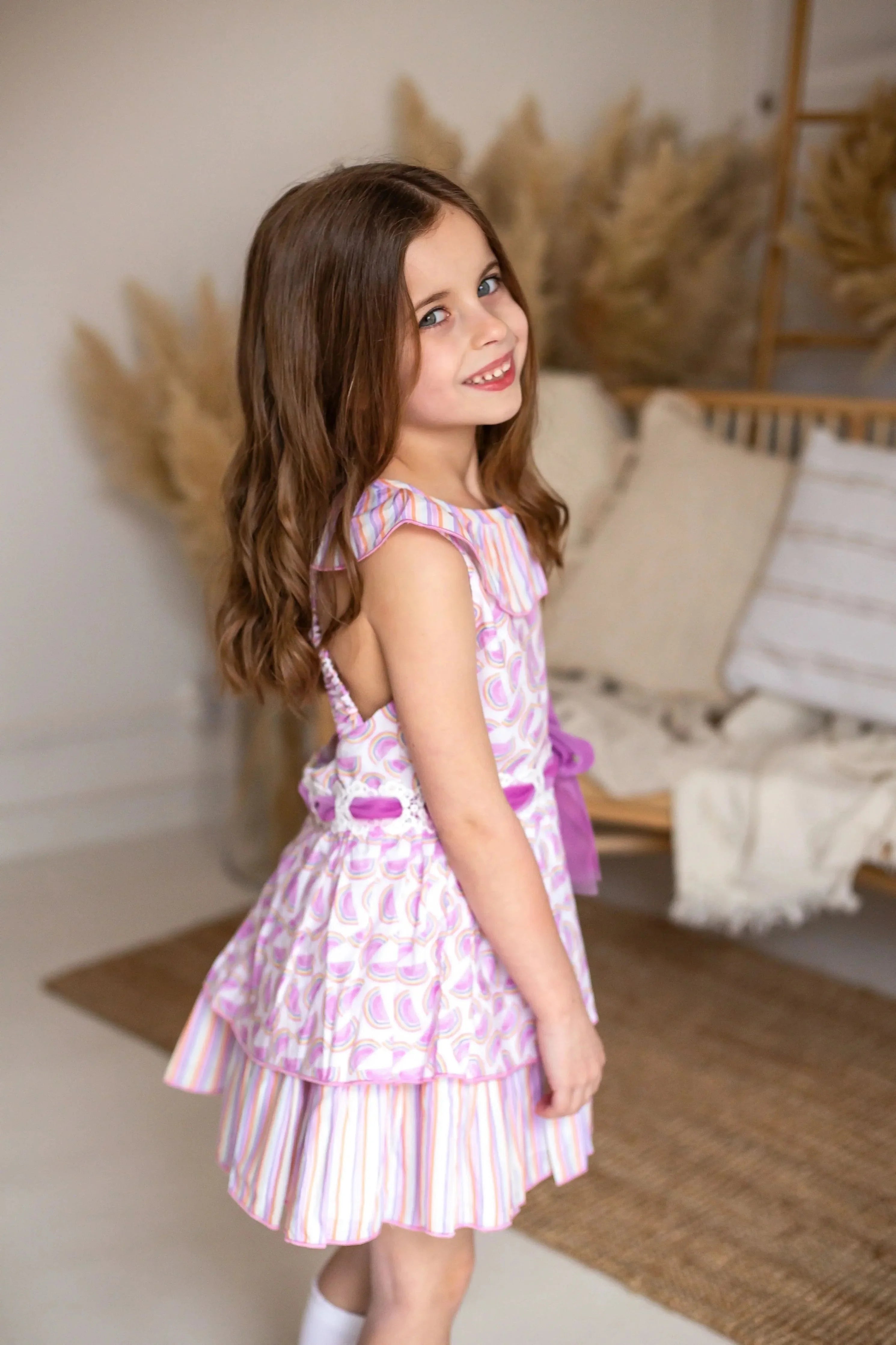 Smiling young girl wearing a pink patterned dress in a cozy, neutral-toned living room